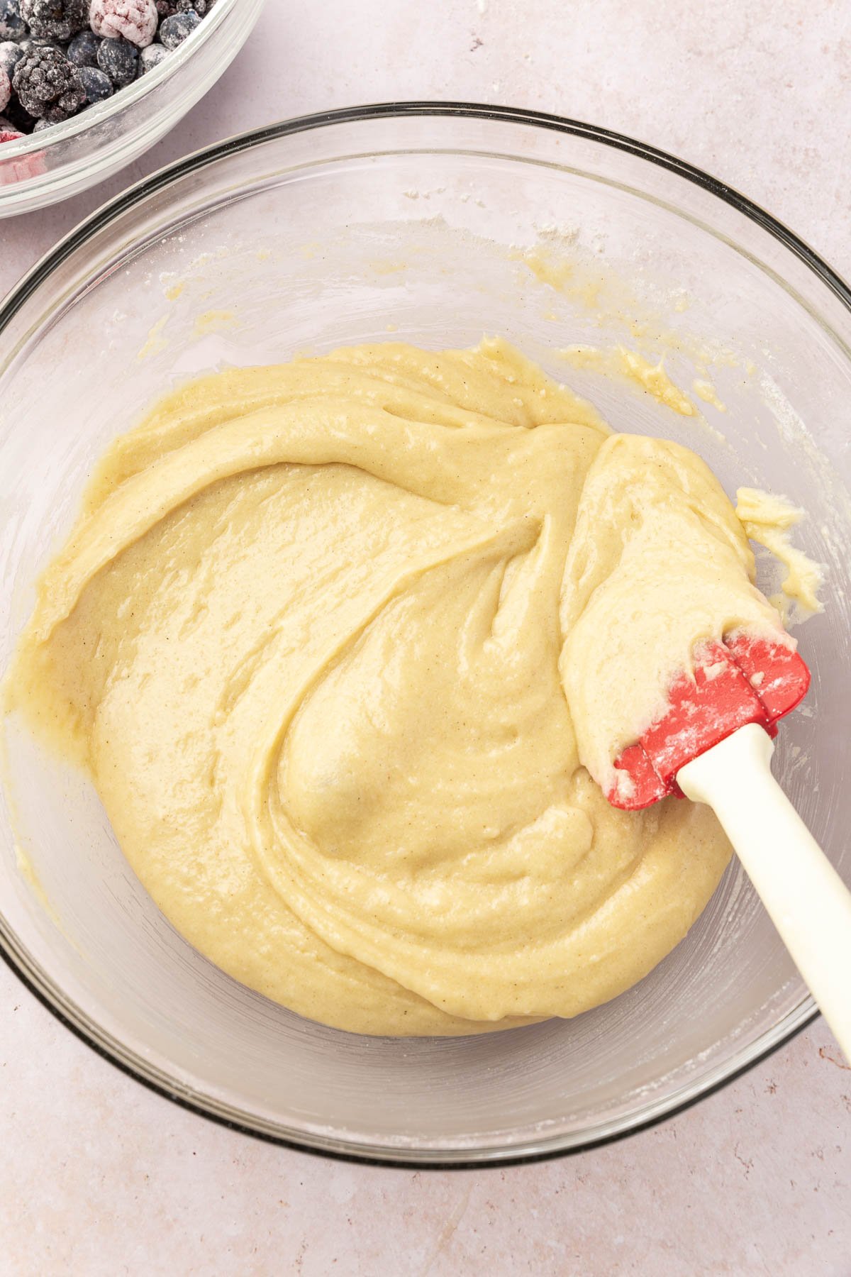 A glass mixing bowl with gluten-free muffin batter in it being stirred by a rubber spatula.