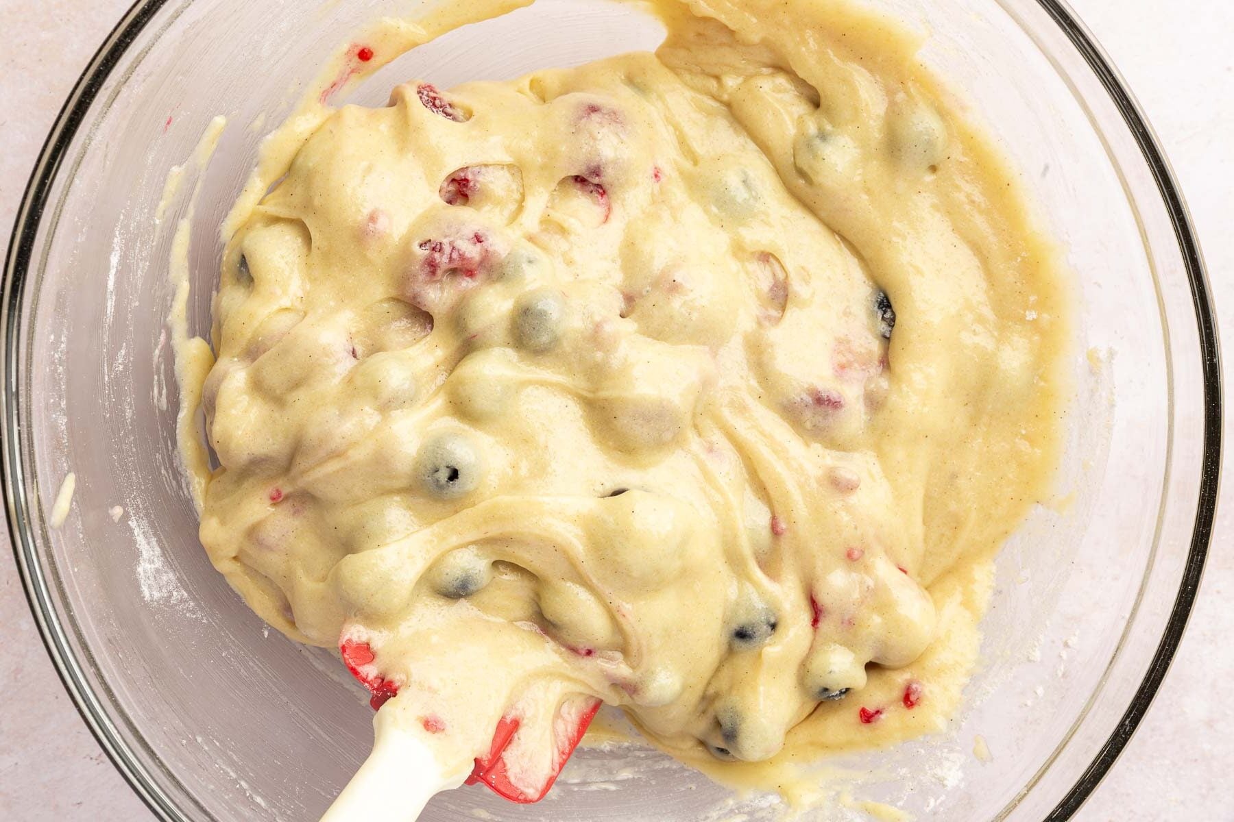 A glass mixing bowl with gluten-free muffin batter with raspberries, blueberries and blackberries folded into it.