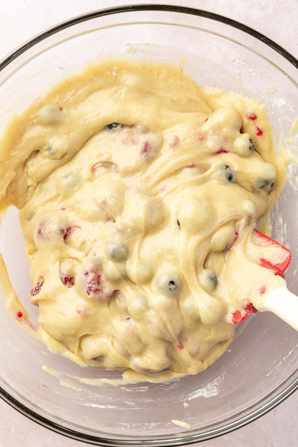 A glass mixing bowl with gluten-free muffin batter with raspberries, blueberries and blackberries folded into it.