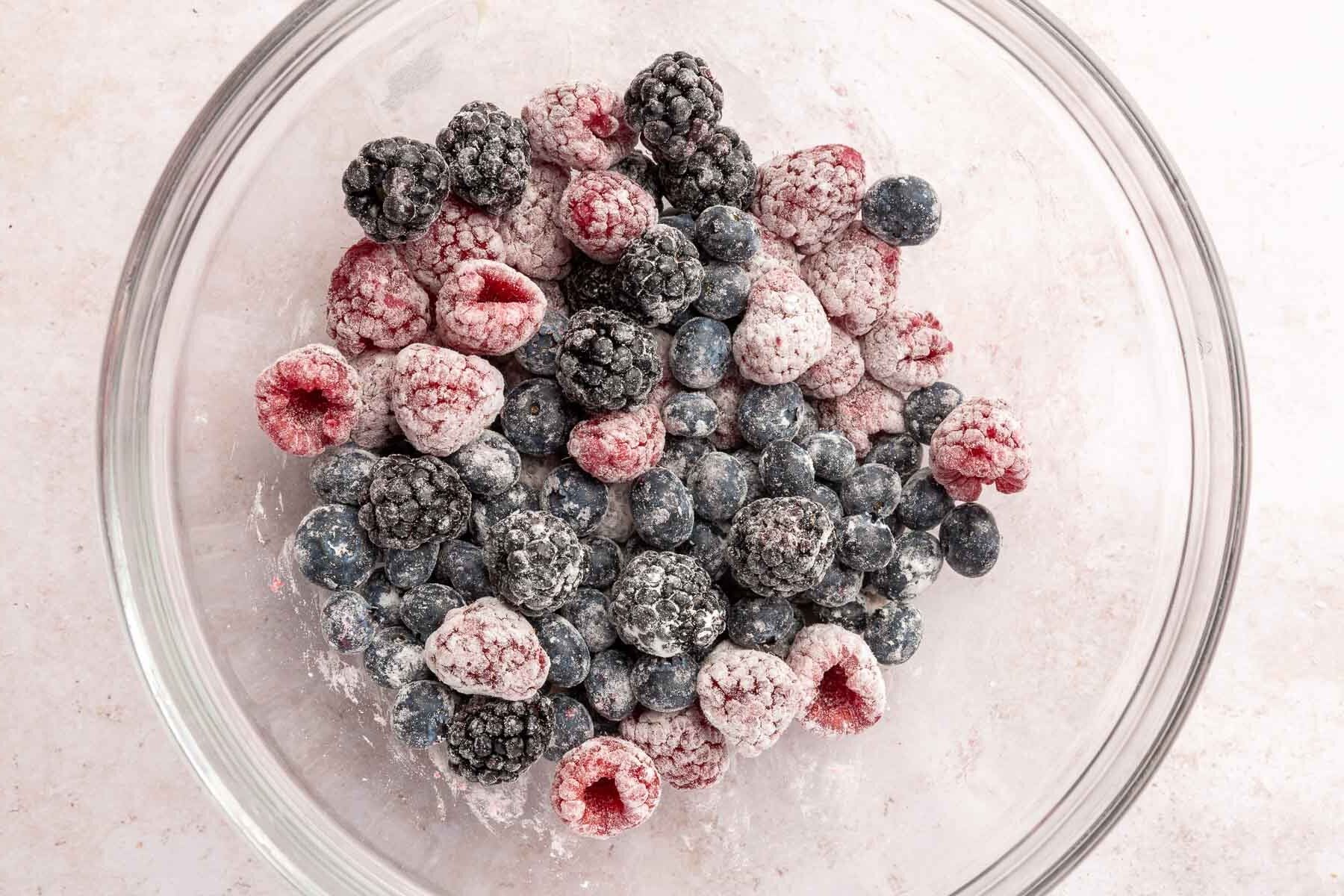 A glass mixing bowl with blueberries, blackberries and raspberries tossed in gluten-free flour.