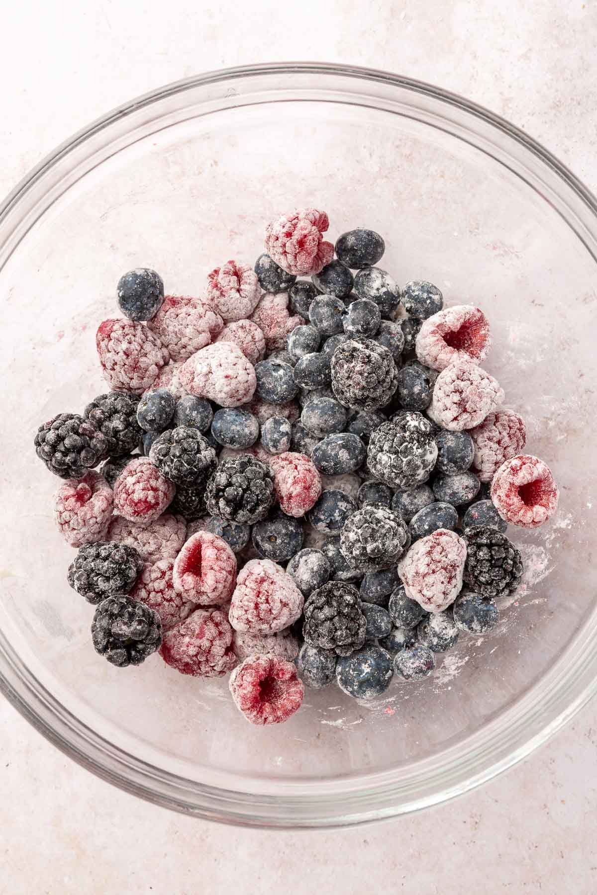 A glass mixing bowl with blueberries, blackberries and raspberries tossed in gluten-free flour.