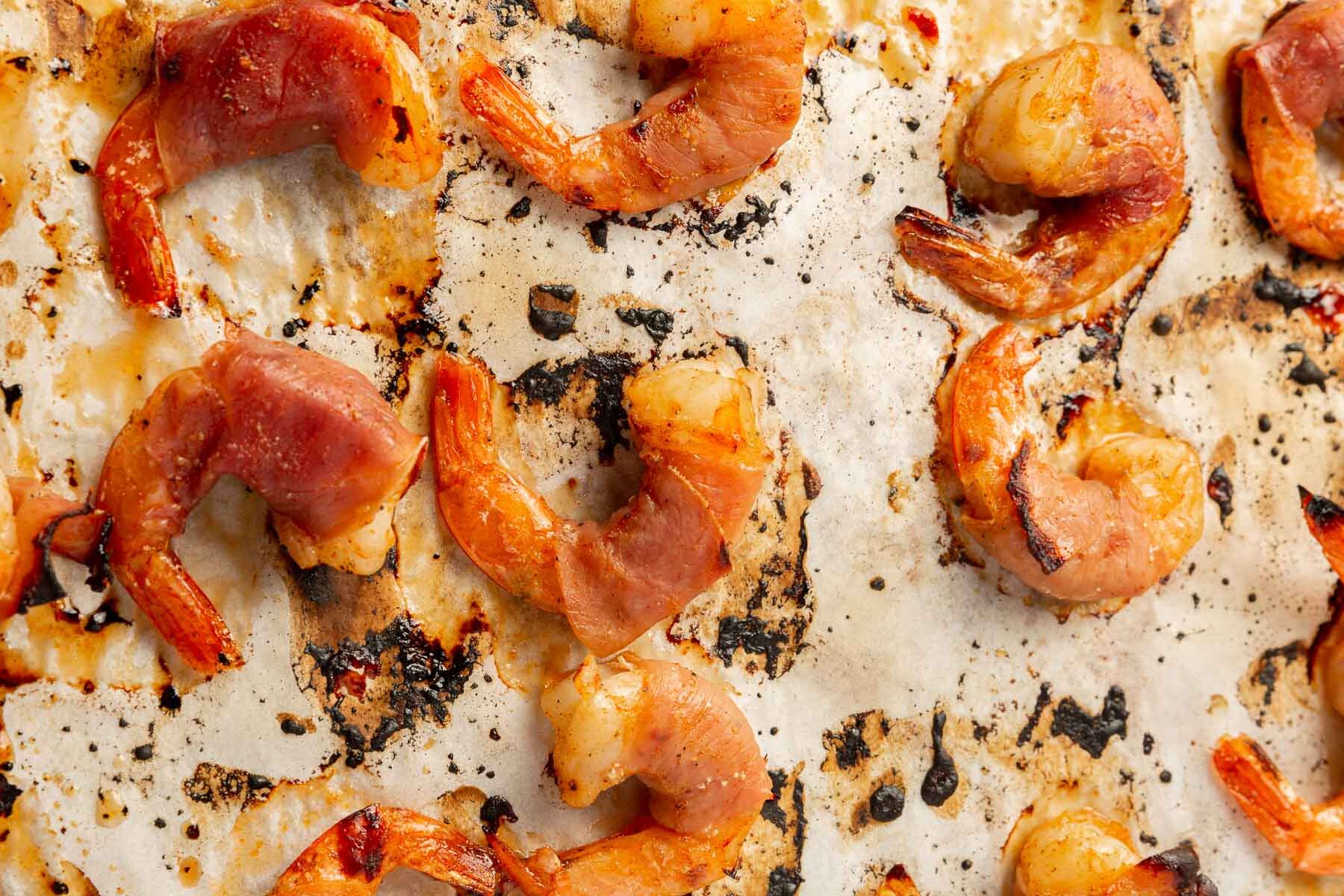 A close up of baked prosciutto wrapped shrimp on a baking sheet lined with parchment paper.
