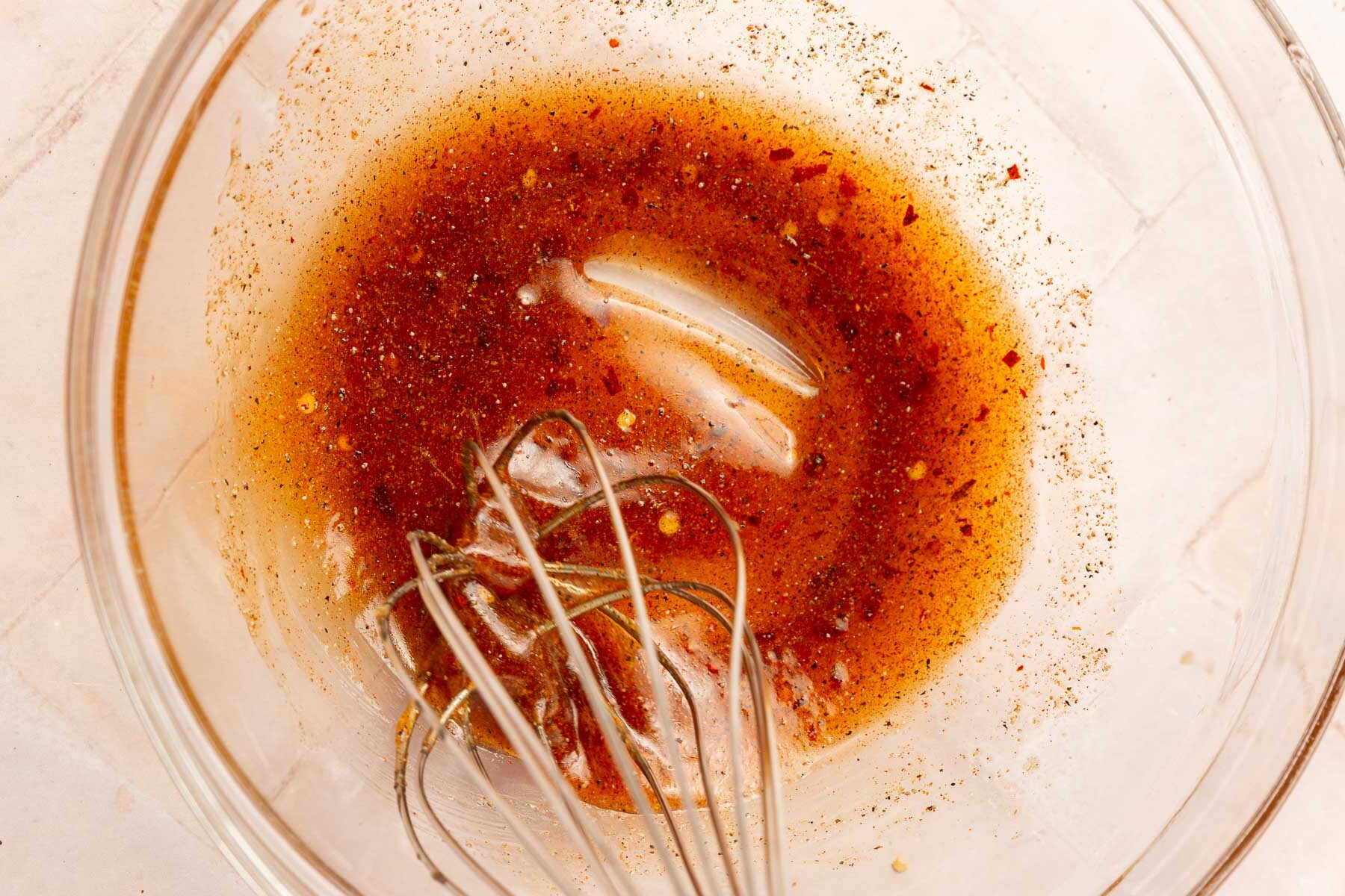 A glass mixing bowl with a honey garlic marinade being whisked together with a wire whisk.