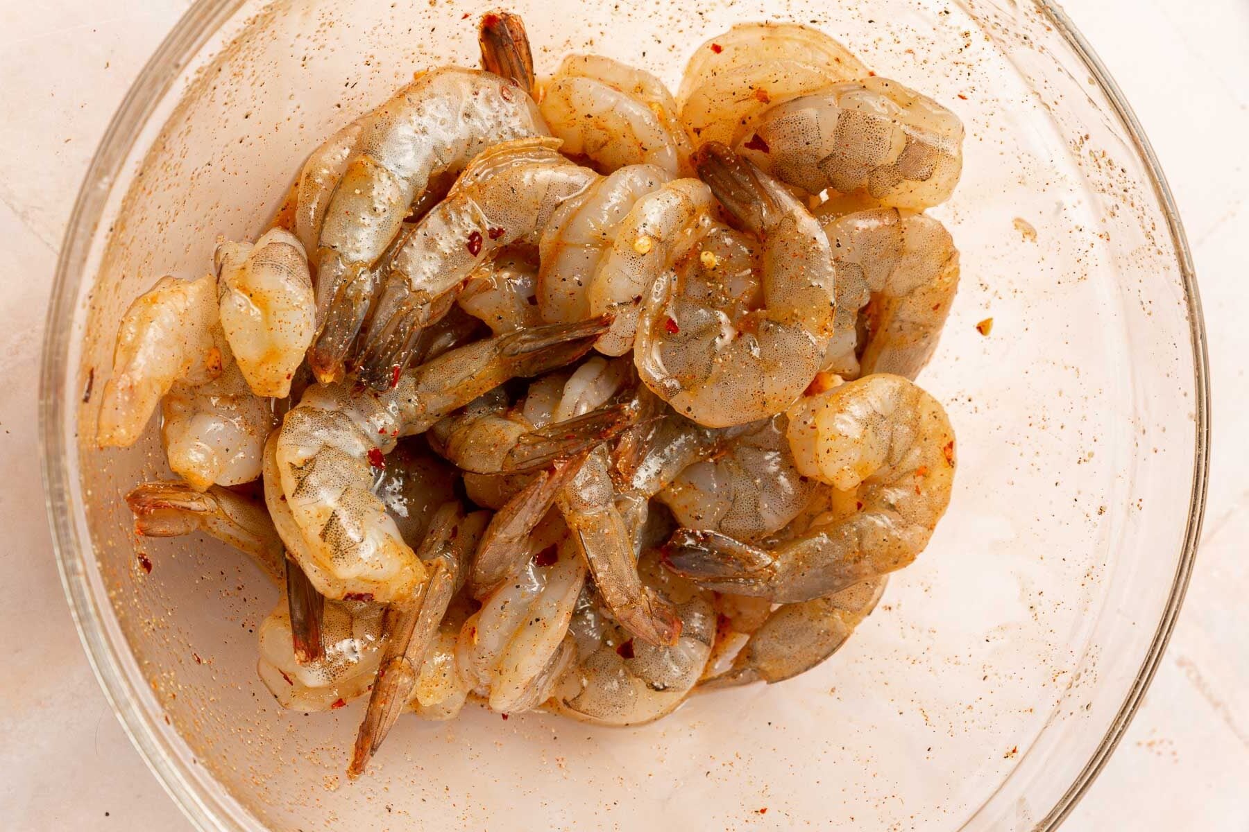 A glass mixing bowl of raw shrimp that has been tossed in a honey garlic marinade.