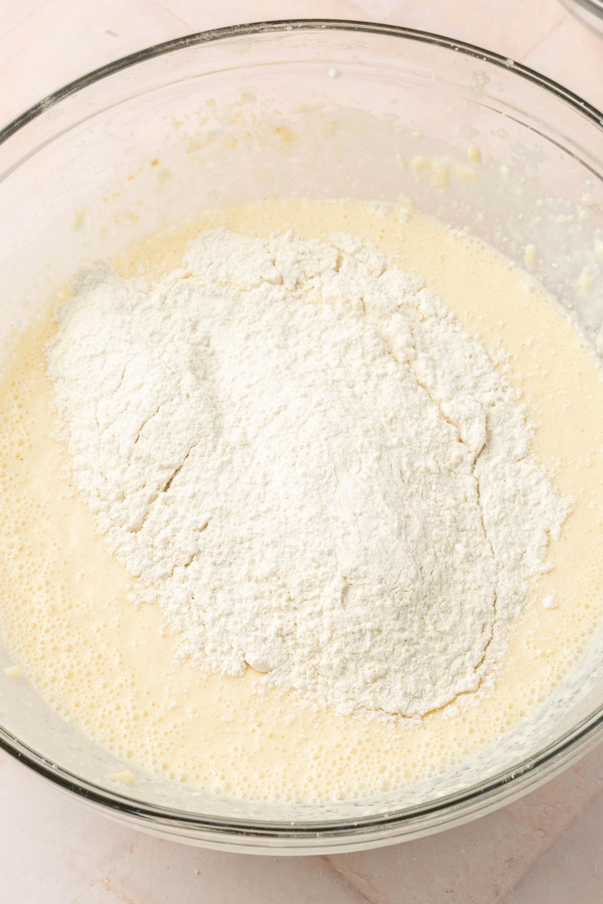A glass mixing bowl with gluten-free flour poured on top of a wet batter to make gluten-free coffee cake.