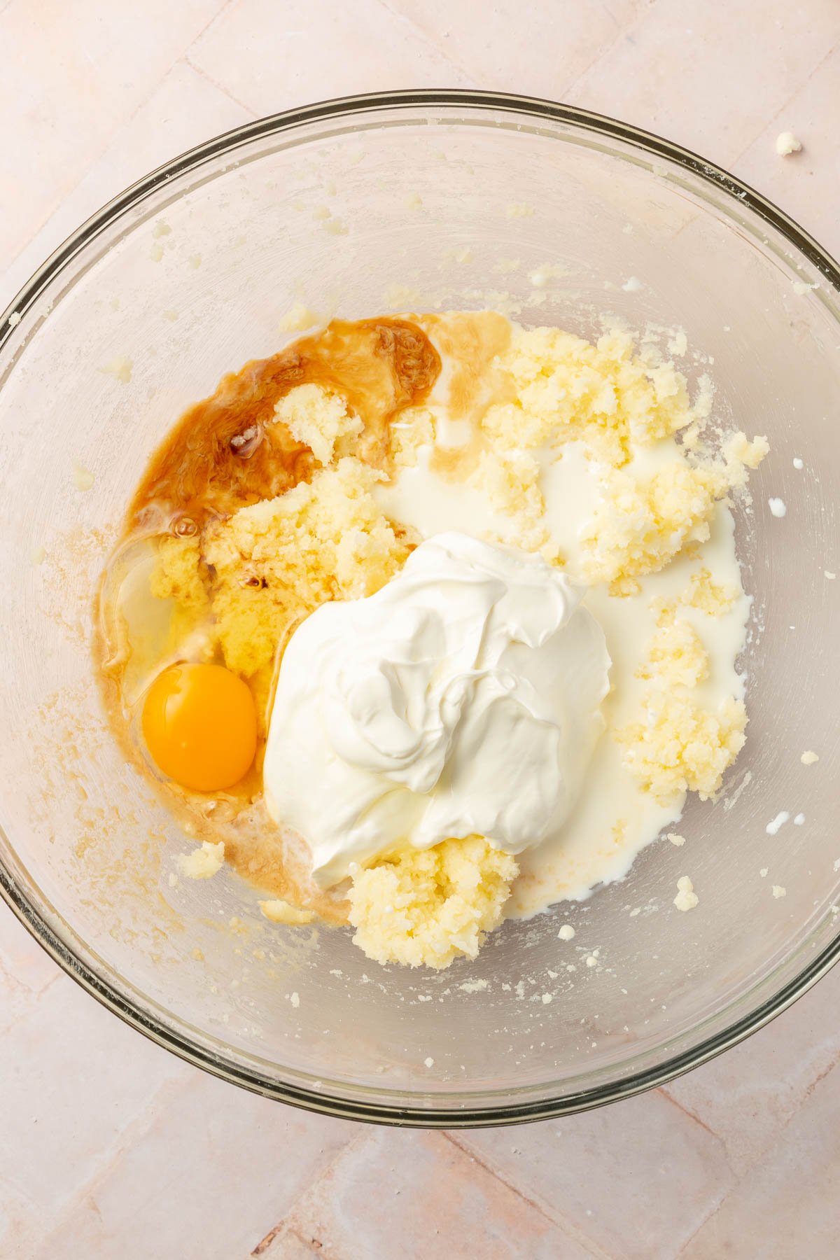 A glass mixing bowl with creamed butter and sugar, sour cream, egg, vanilla extract and milk before mixing together.