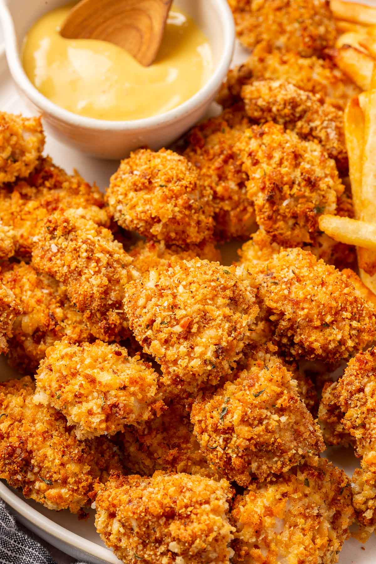 A close up of a pile of gluten free chicken nugets on a plate with a ramekin of honey mustard dipping sauce with a small spoon in it.