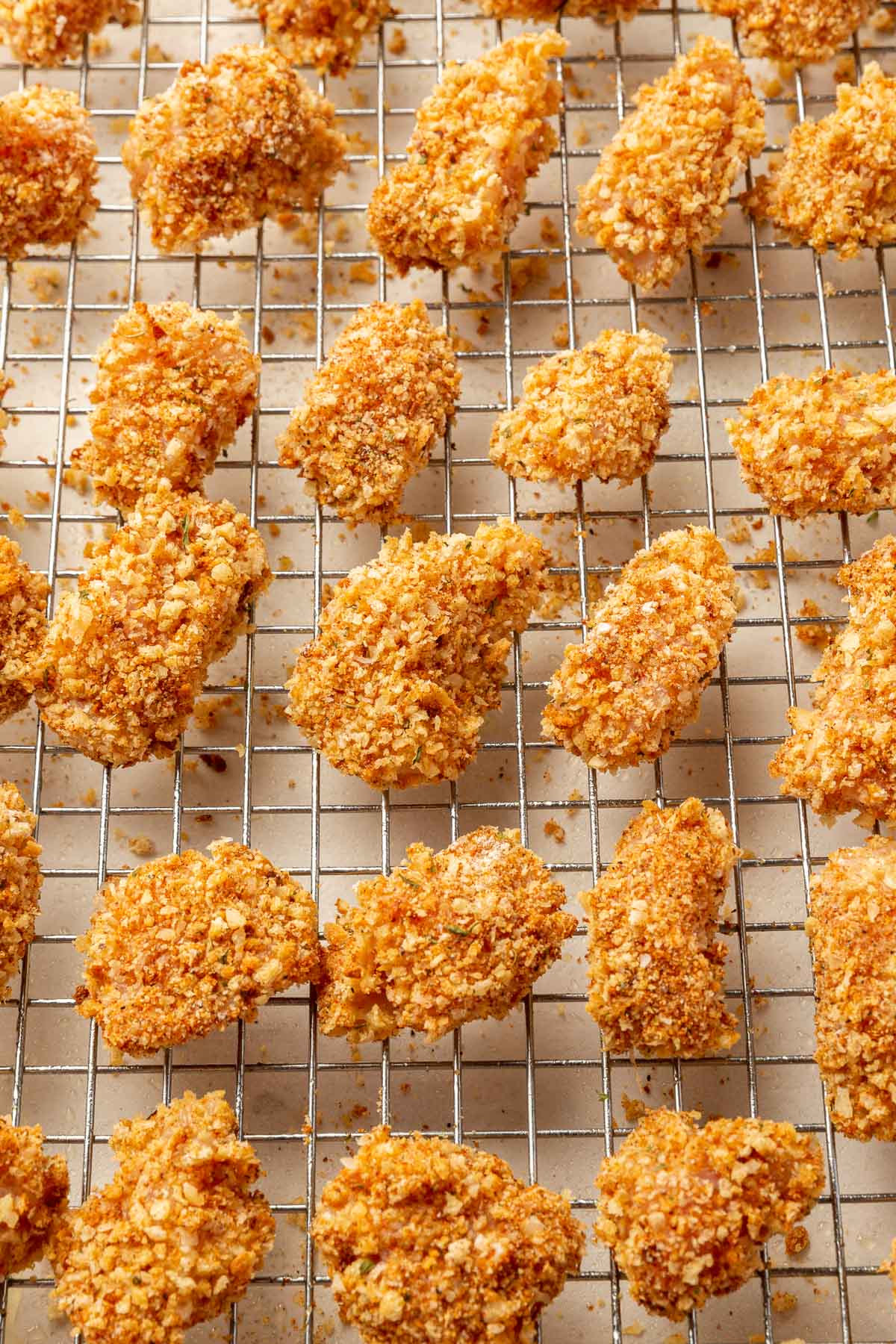 Gluten-free chicken nuggets lined up in rows on a wire cooling rack over a baking sheet before baked in the oven.