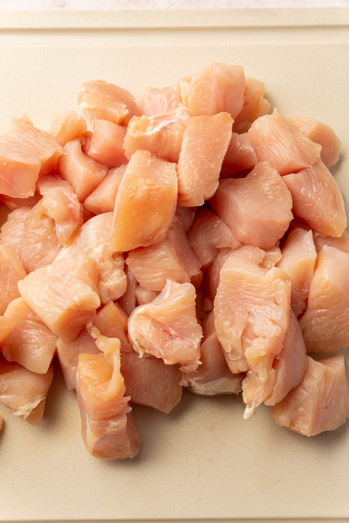 A cutting board of chicken breasts that have been cut into 1-inch cubes.
