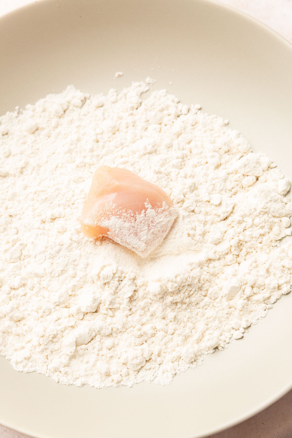 A chicken cube being coated in a bowl of gluten-free flour.