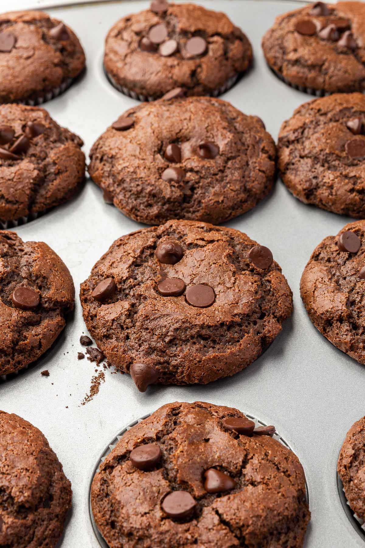 Close-up of a muffin tin filled with freshly baked gluten-free chocolate muffins, highlighting the texture and chocolate chips on top of each muffin.