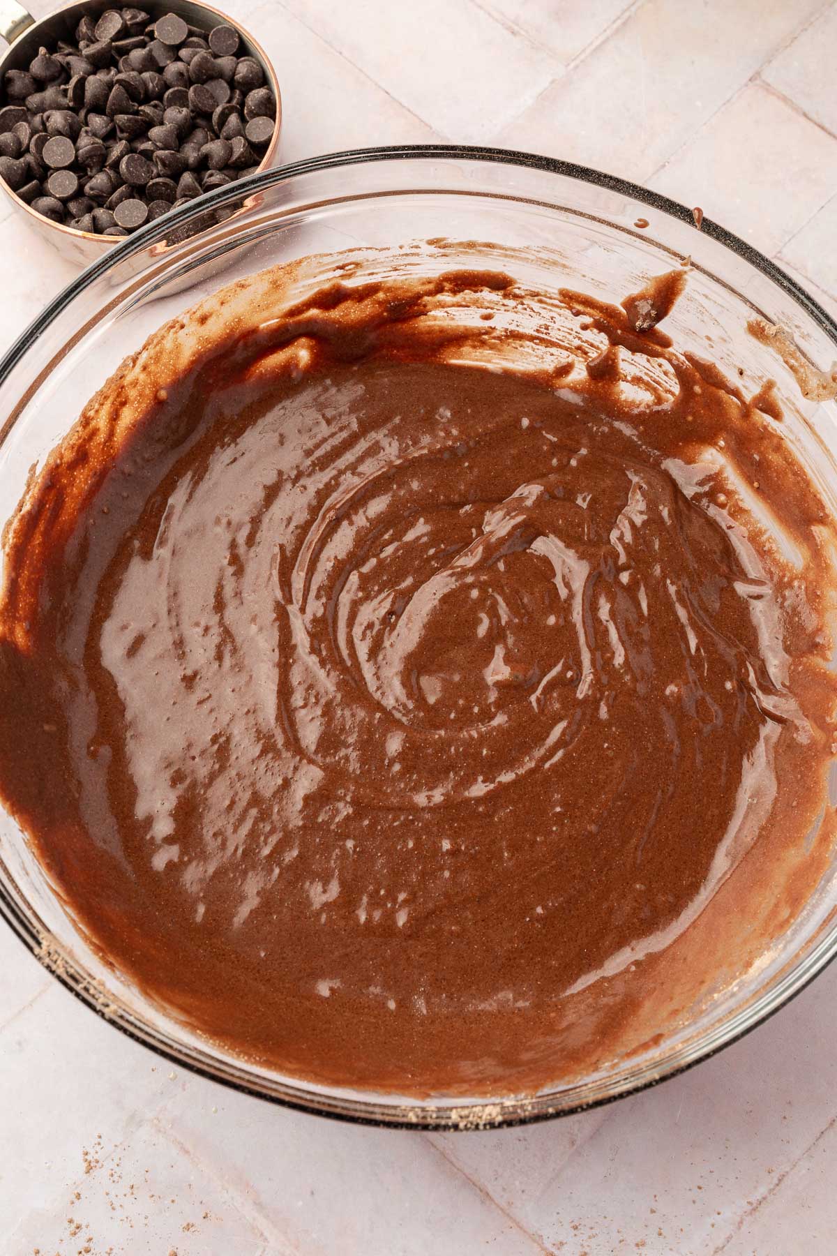 A mixing bowl filled with a smooth, thick chocolate batter, ready for gluten-free chocolate muffins, with a small bowl of chocolate chips beside it.