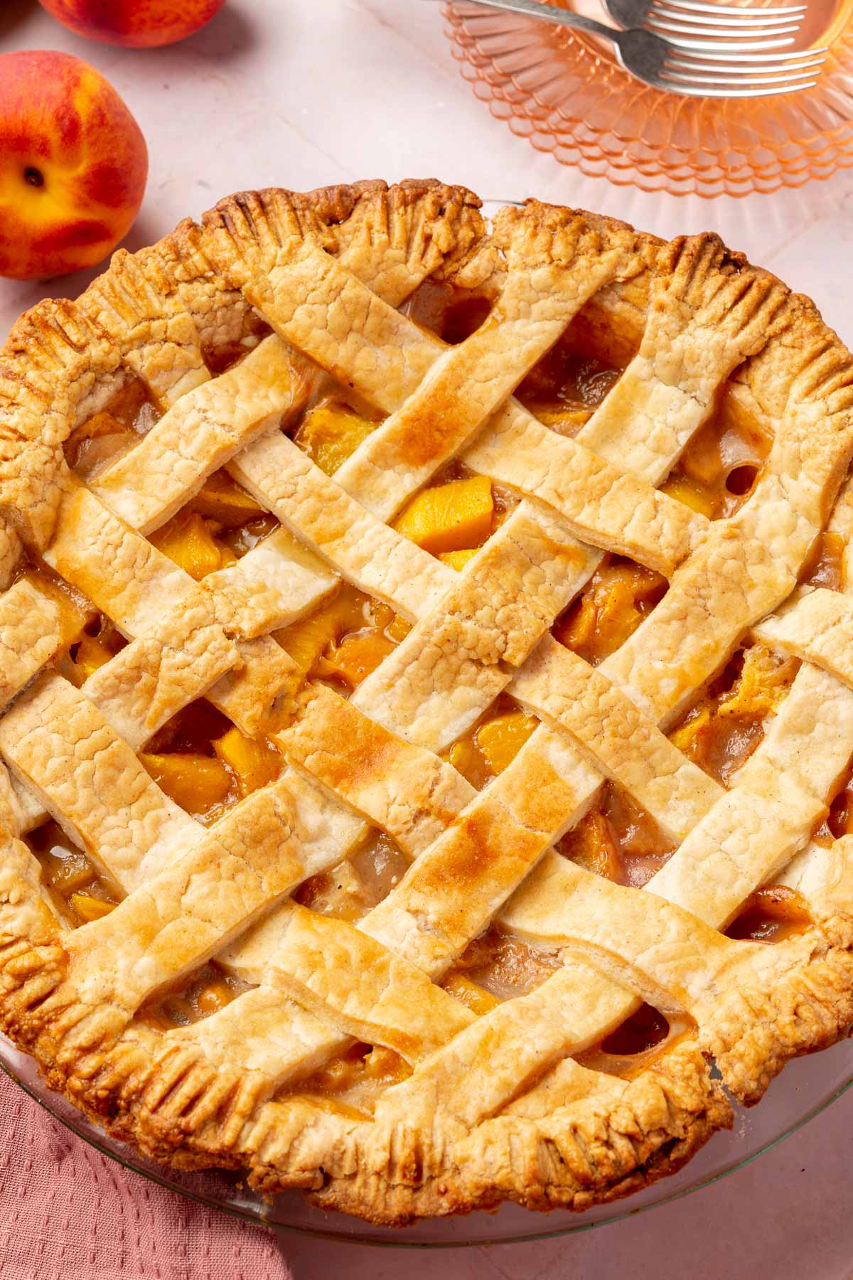 A close up of a gluten-free peach mango pie with lattice top with dessert plates and forks in the background.