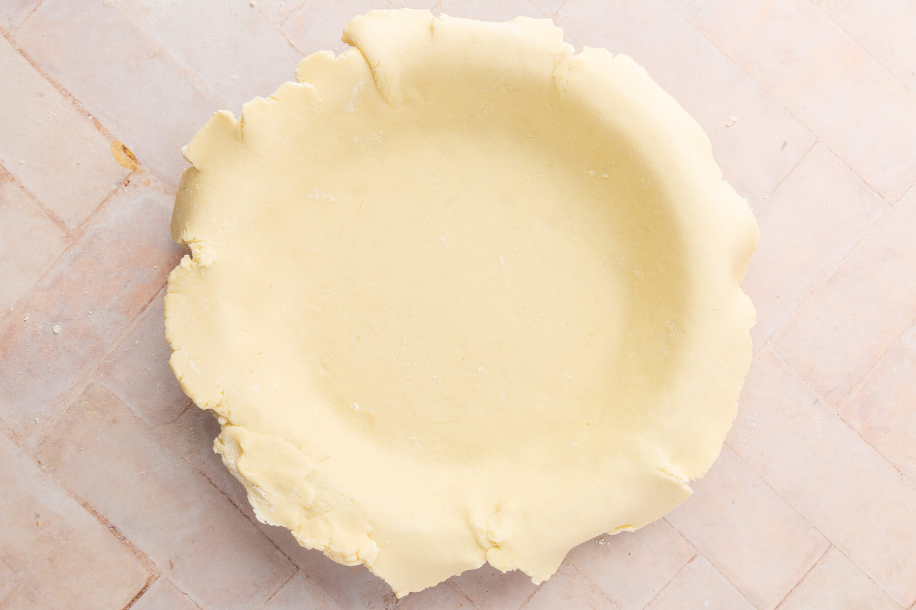 An unbaked gluten-free pie crust laid into a pie pan with the edges slightly overhanging.