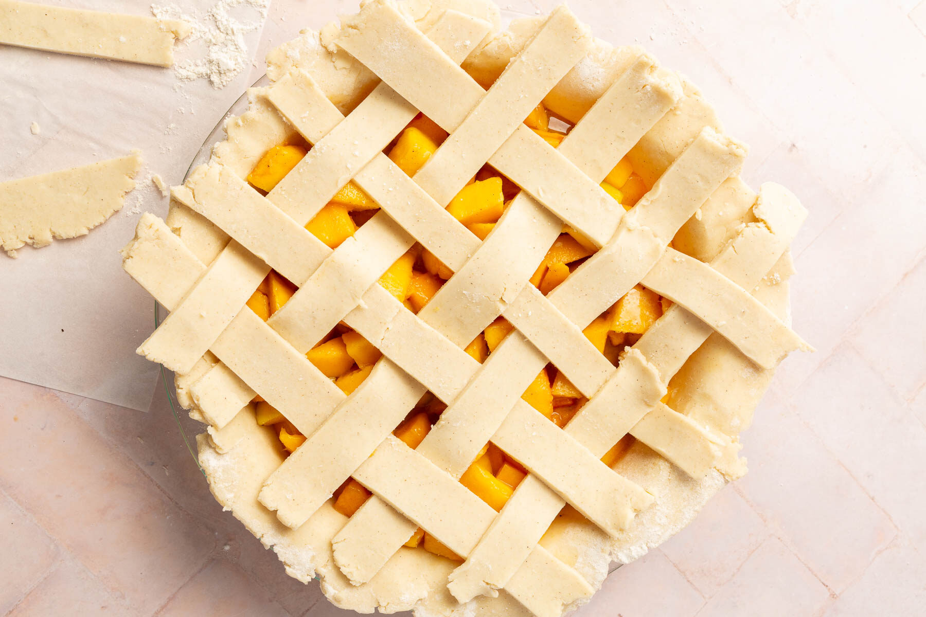 An overhead view of an unbaked gluten-free peach mango pie with a lattice pie crust.
