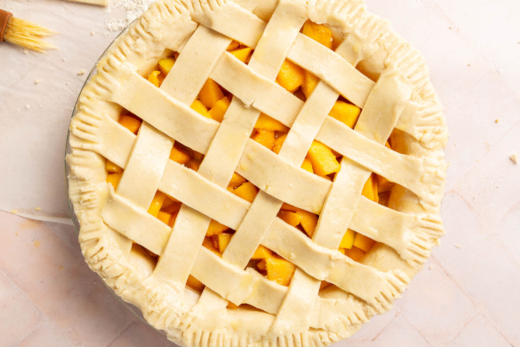 An overhead view of an unbaked gluten-free peach mango pie with a lattice pie crust that has been brushed with egg wash before baking in the oven.