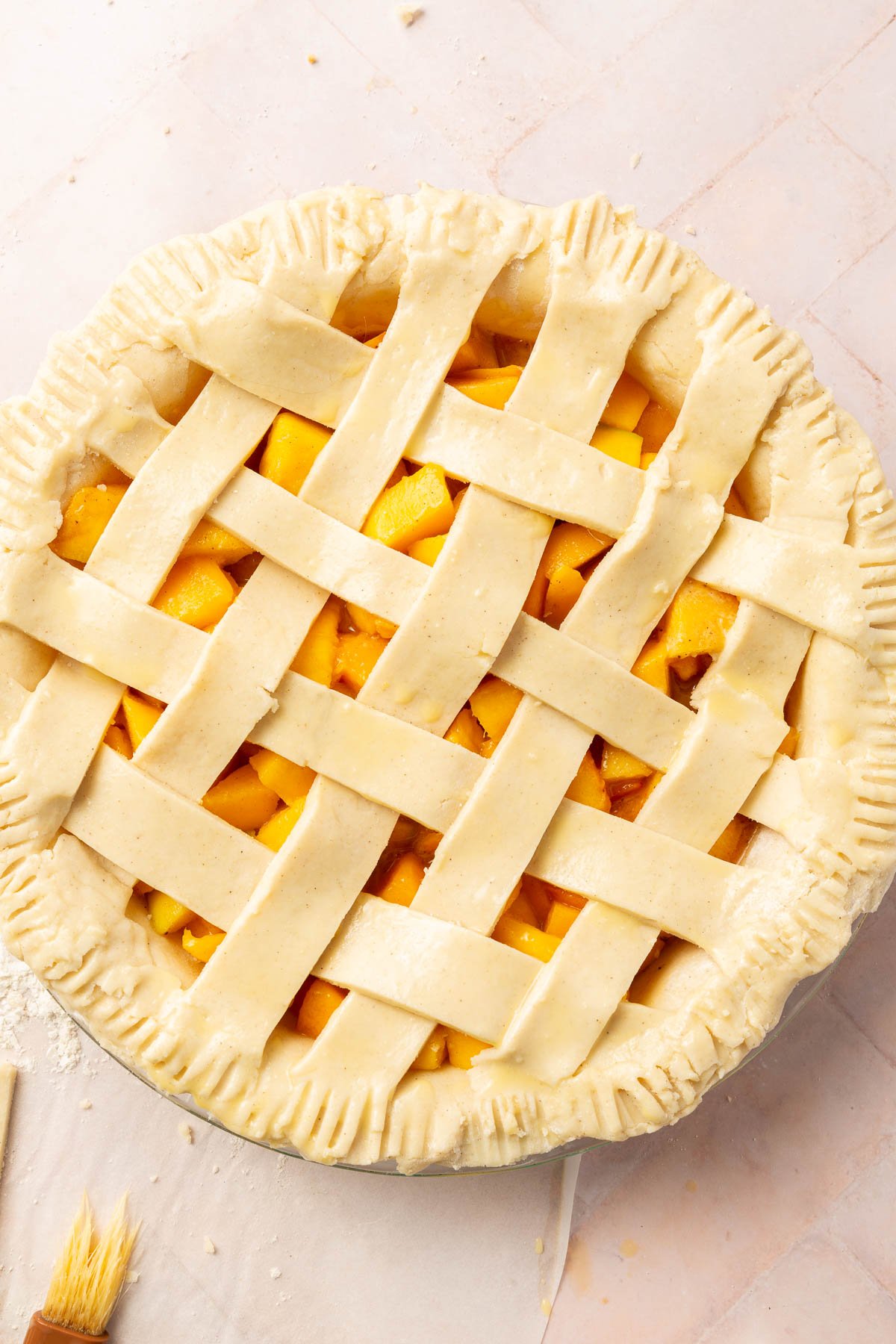 An overhead view of an unbaked gluten-free peach mango pie with a lattice pie crust that has been brushed with egg wash before baking in the oven.