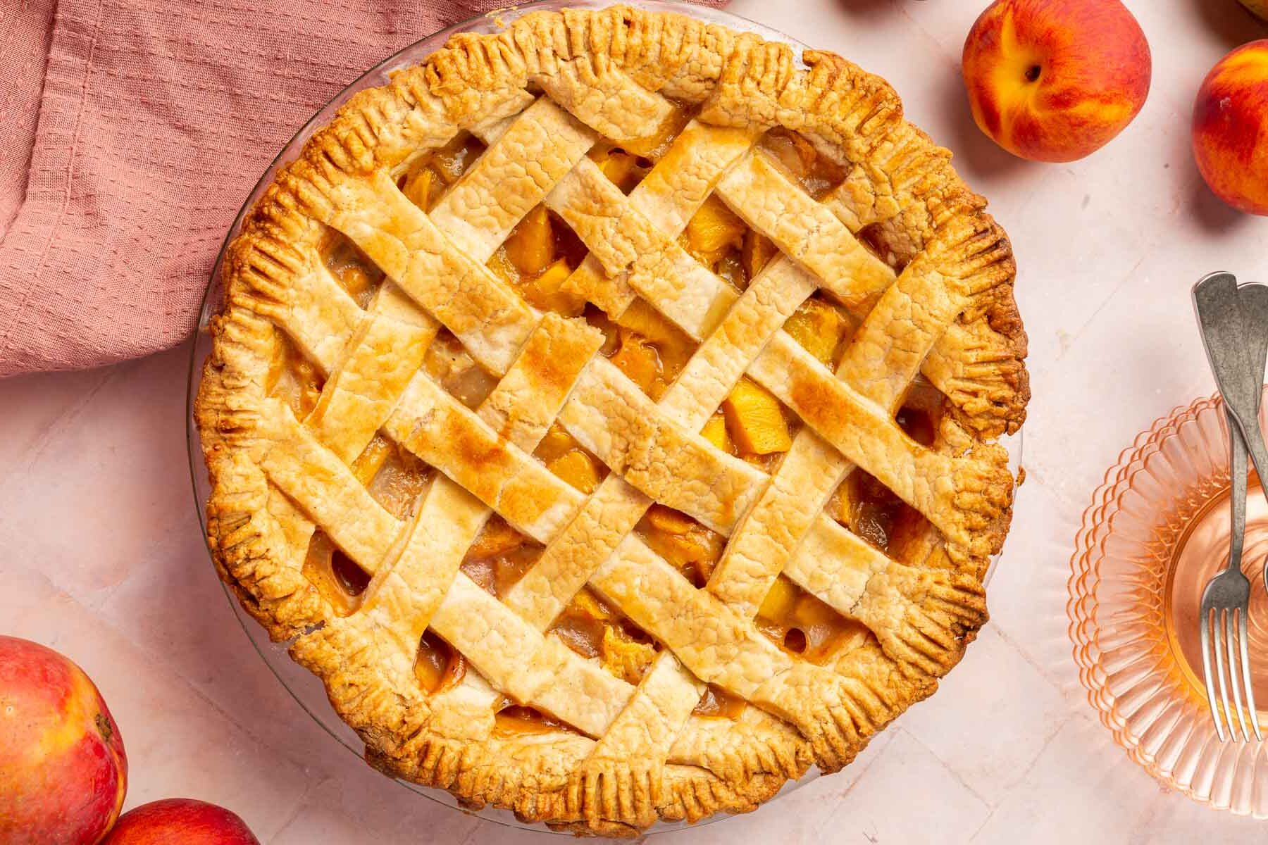 An overhead view of a gluten-free peach mango pie with a lattice crust and fresh peaches surrounding the pie.