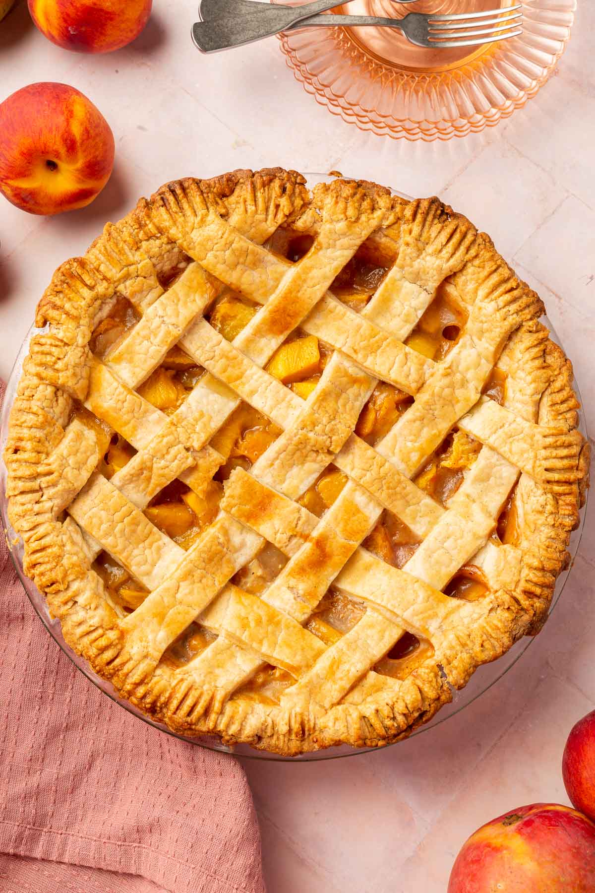 An overhead view of a gluten-free peach mango pie with a lattice crust and fresh peaches surrounding the pie.