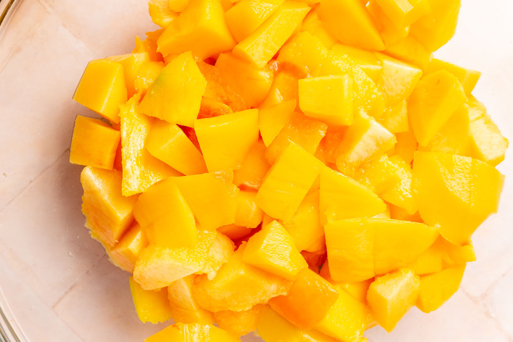 A glass mixing bowl with diced peaches and mango in it.