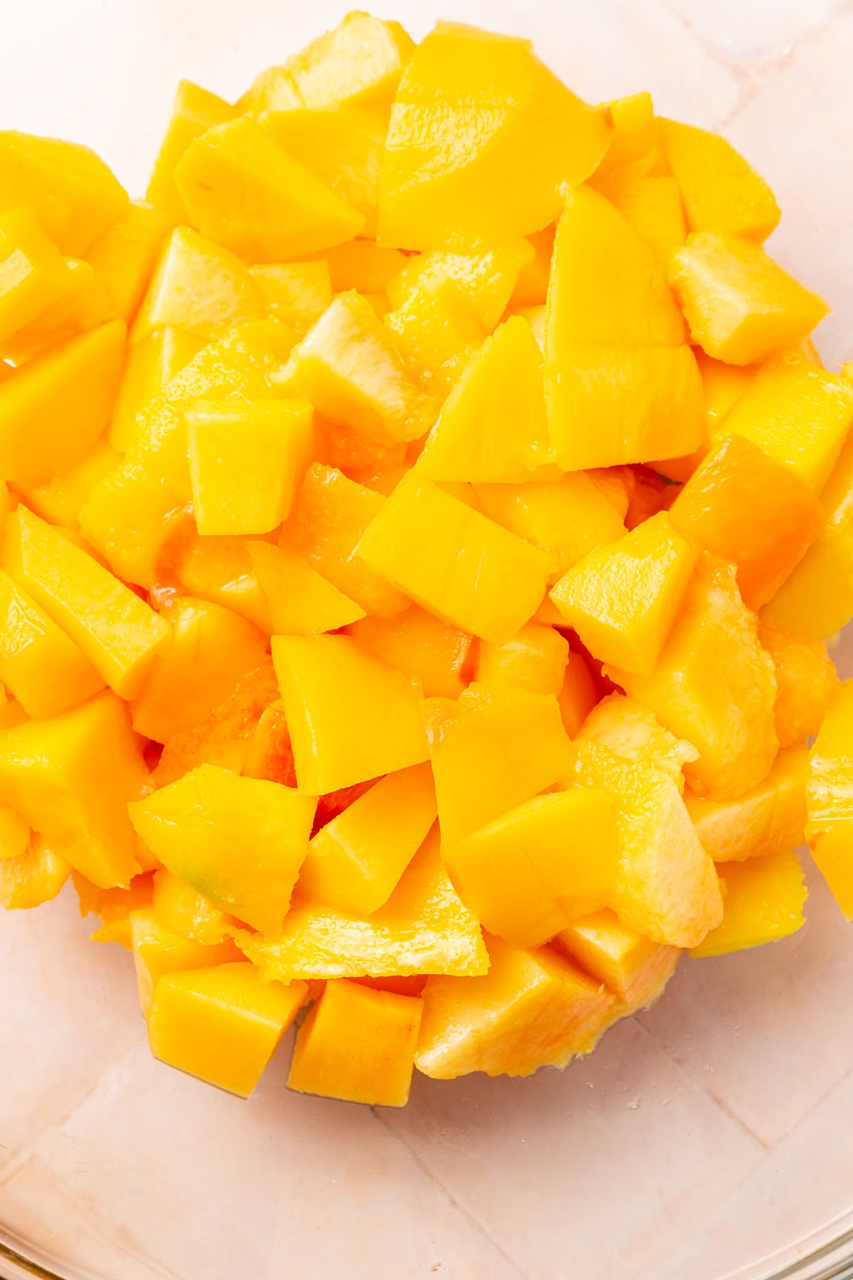 A glass mixing bowl with diced peaches and mango in it.