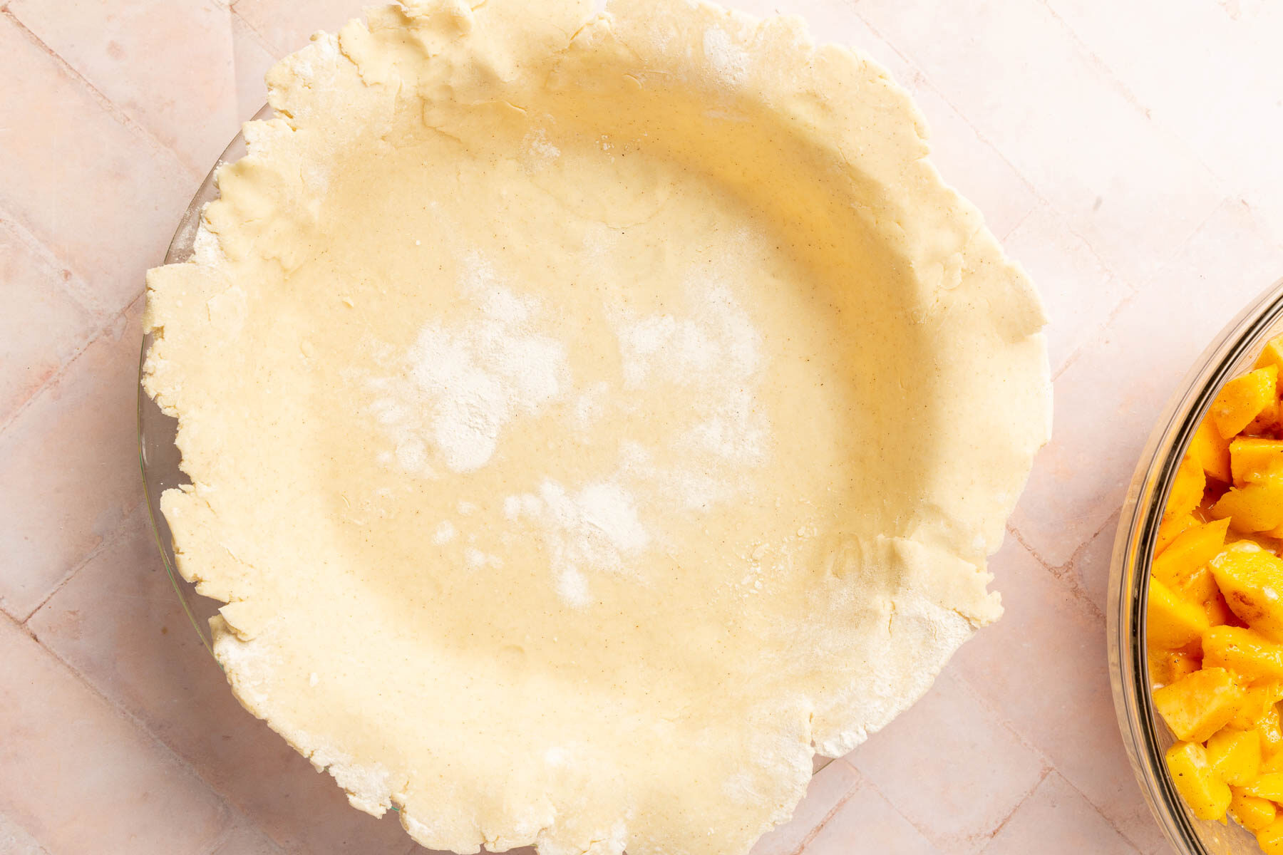 Gluten-free pie dough that has been fit into a 9-inch pie plate with a bowl of peach mango pie filling off to the side.