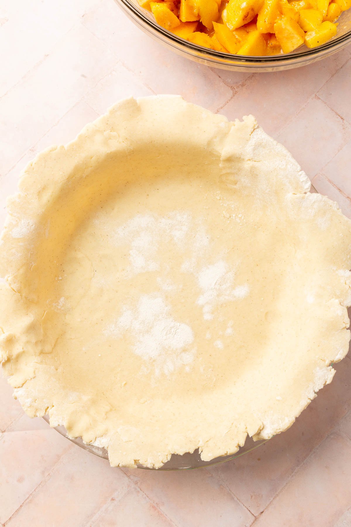 Gluten-free pie dough that has been fit into a 9-inch pie plate with a bowl of peach mango pie filling off to the side.