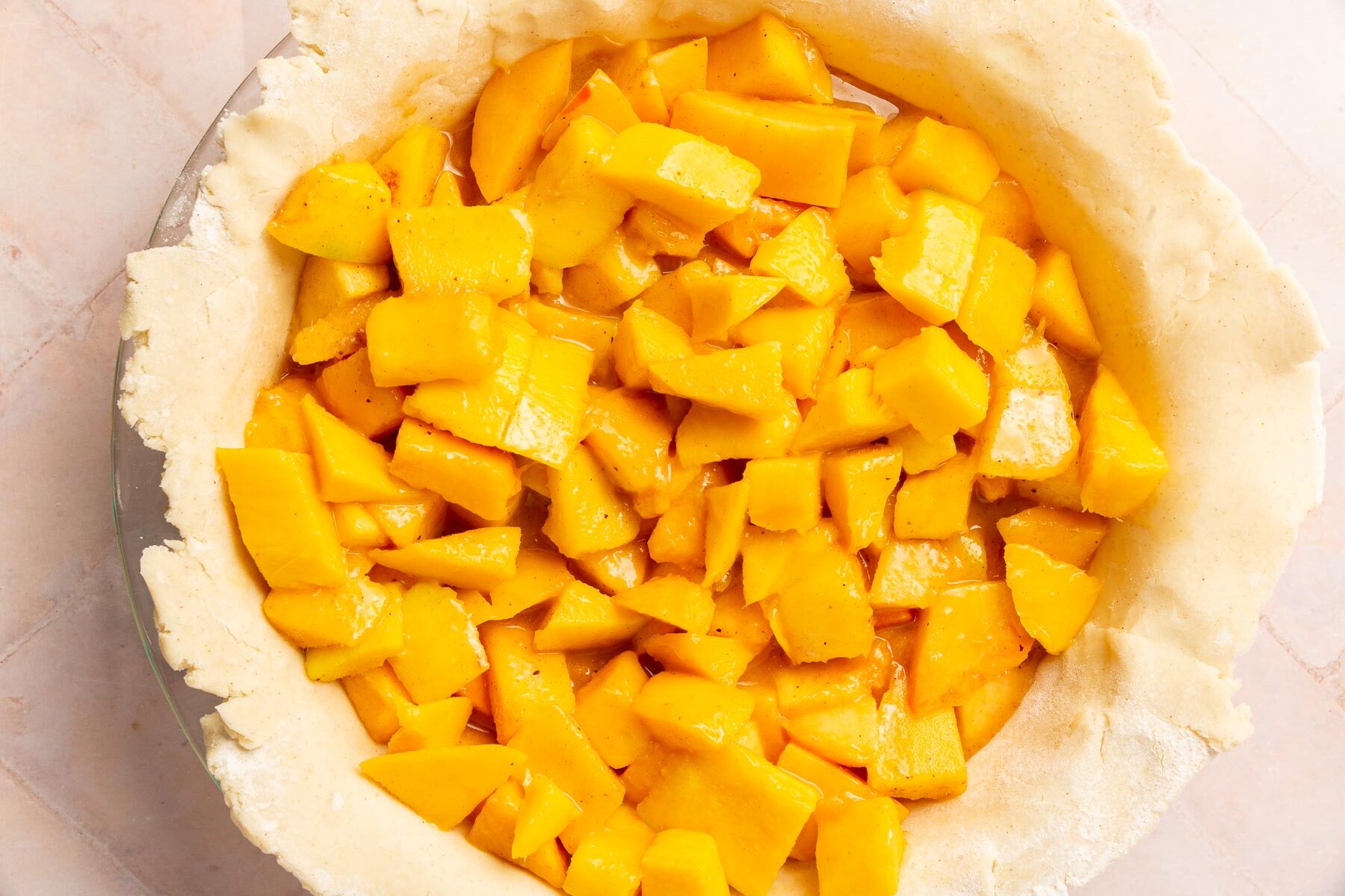 A gluten-free pie dough filled with peach mango pie filling before topping with a top crust and baking In the oven.