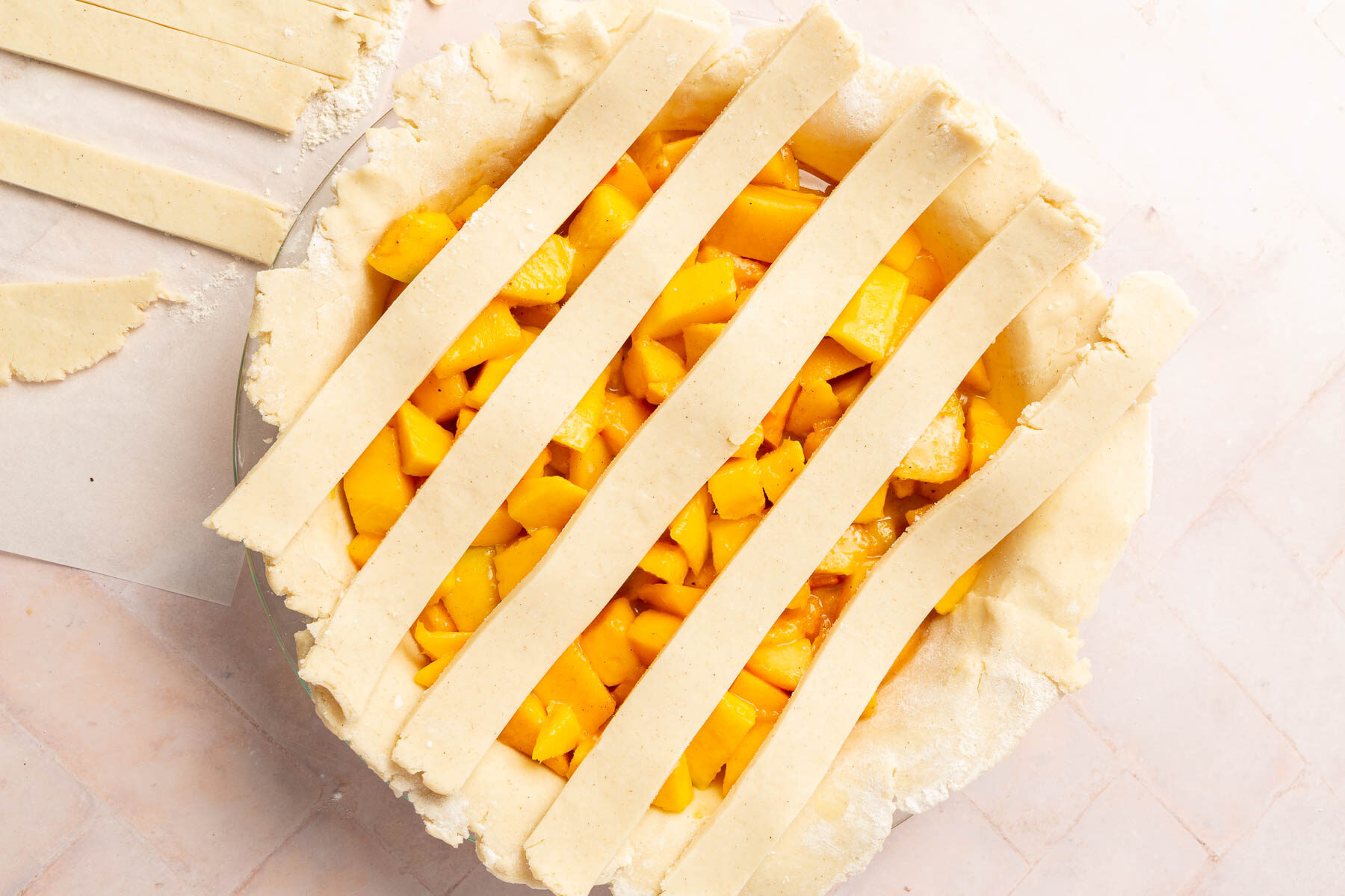 Five strips of gluten-free pie dough on top of a peach mango pie filling to make a lattice pie crust top.