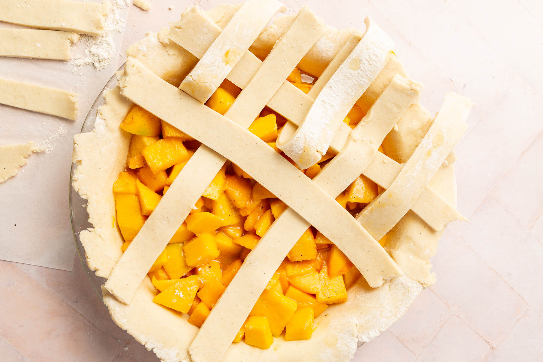 A gluten-free lattice pie dough being weaved on top of a peach mango pie filling.
