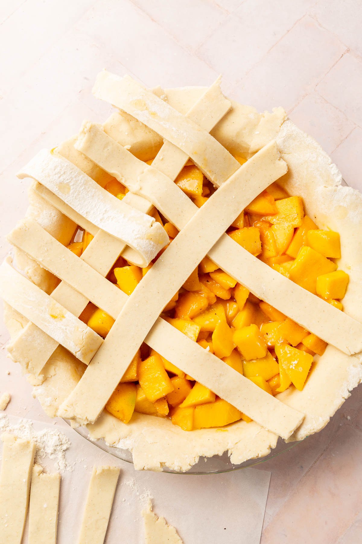 A gluten-free lattice pie dough being weaved on top of a peach mango pie filling.