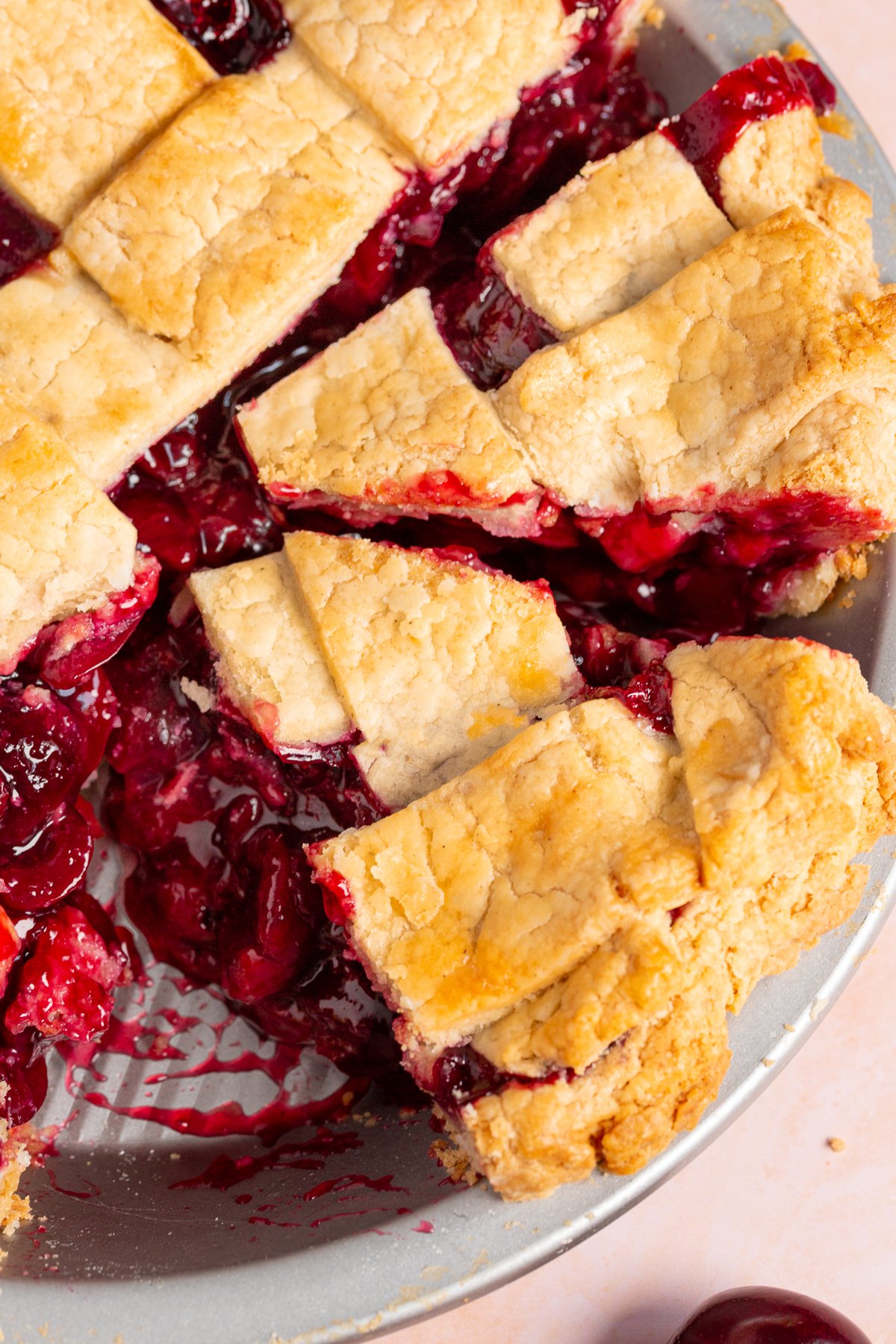 Close-up of a slice of gluten-free cherry pie served on a pink plate, with the cherry filling oozing from under the flaky crust.