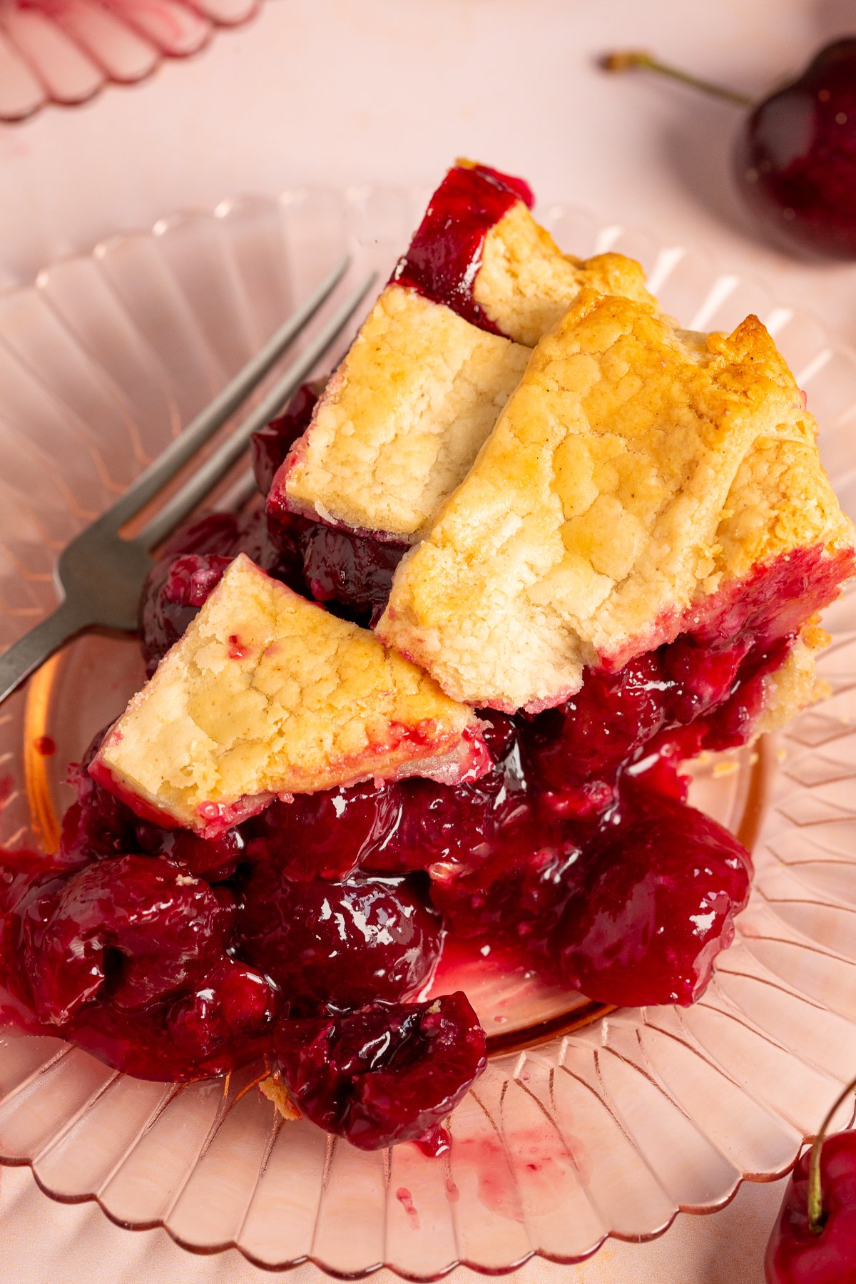 Close-up of a slice of gluten-free cherry pie served on a pink plate, with the cherry filling oozing from under the flaky crust.