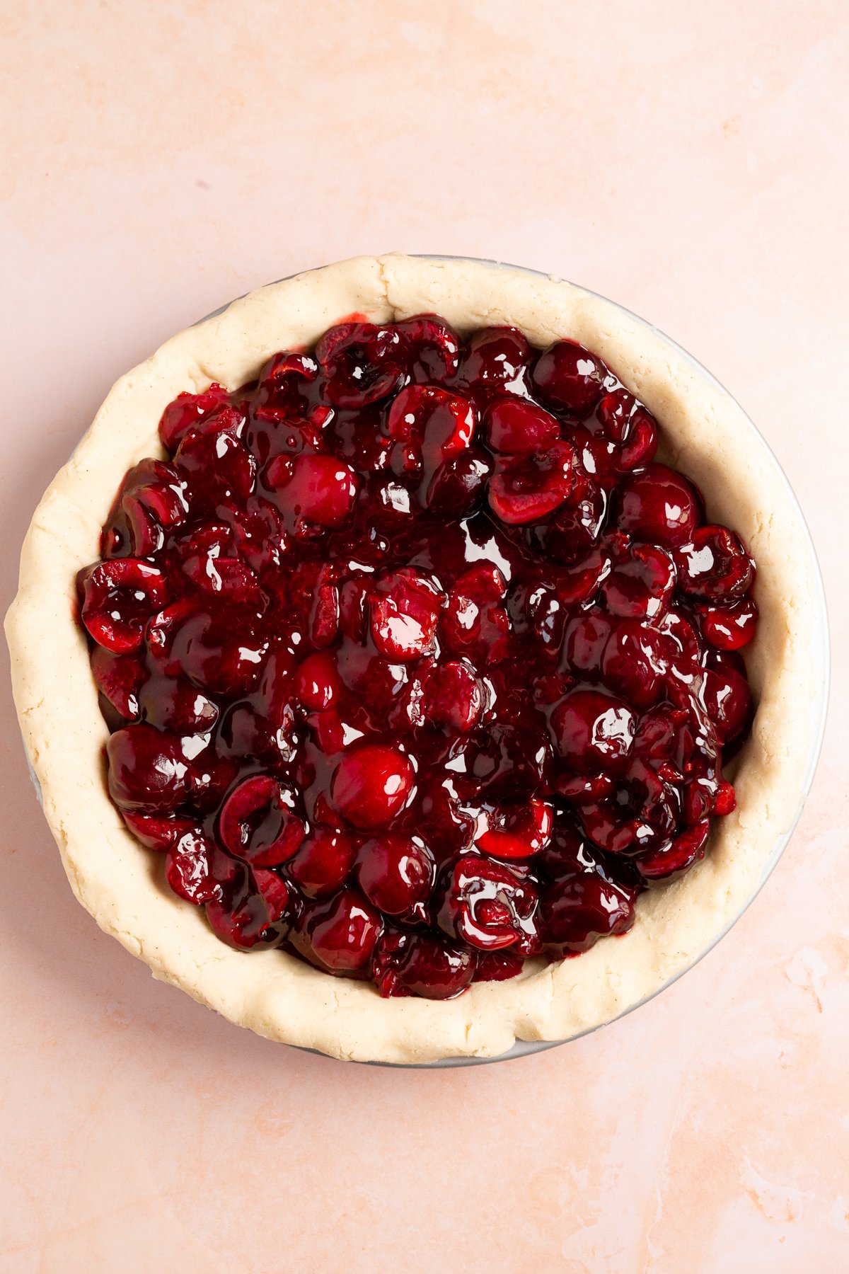 The pie pan filled with rich, glossy cherry pie filling, ready for the top crust to be added.