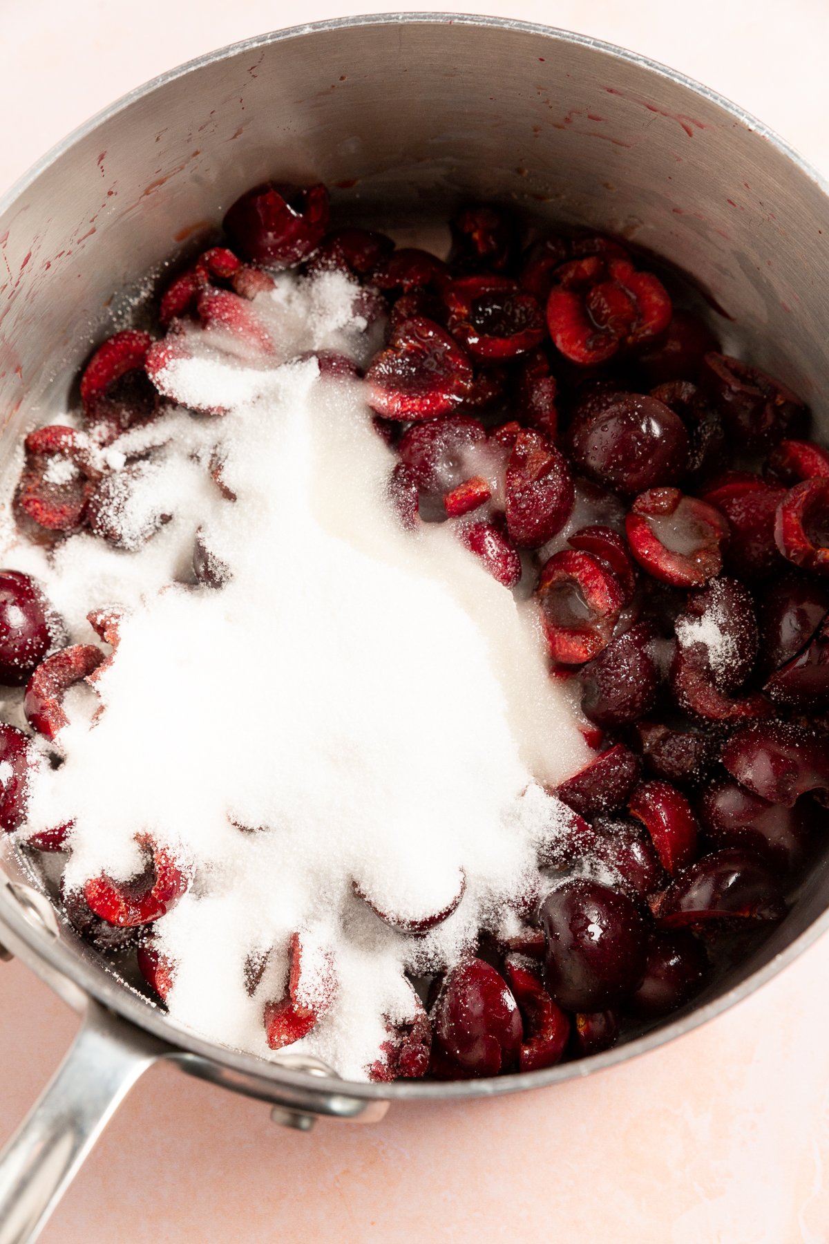 A saucepan filled with pitted cherries and granulated sugar, prepared for cooking the cherry pie filling.