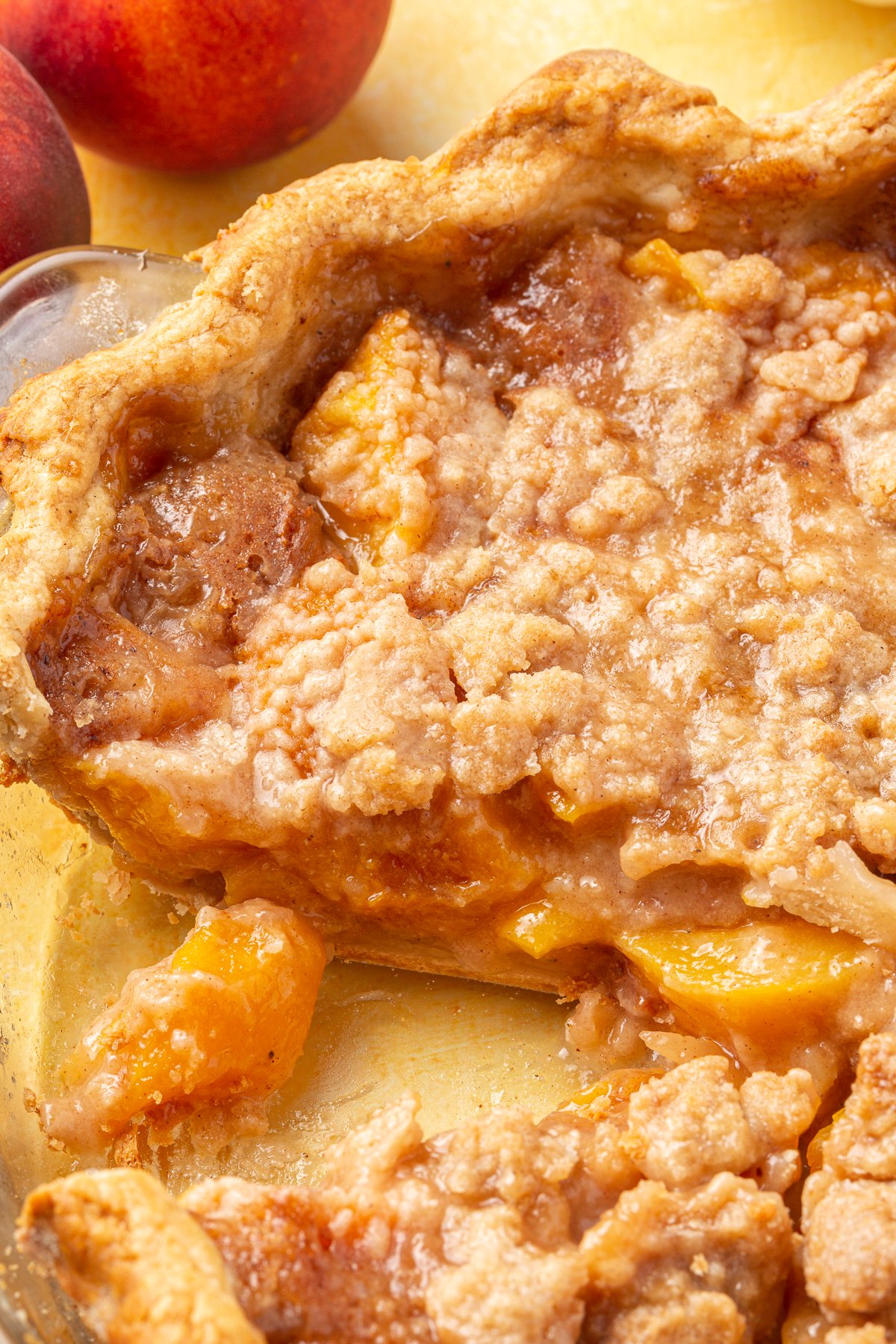 A close-up of the gluten-free peach crumble pie, showing the golden crust and soft peach filling with crumbly topping wit a slice missing from it.