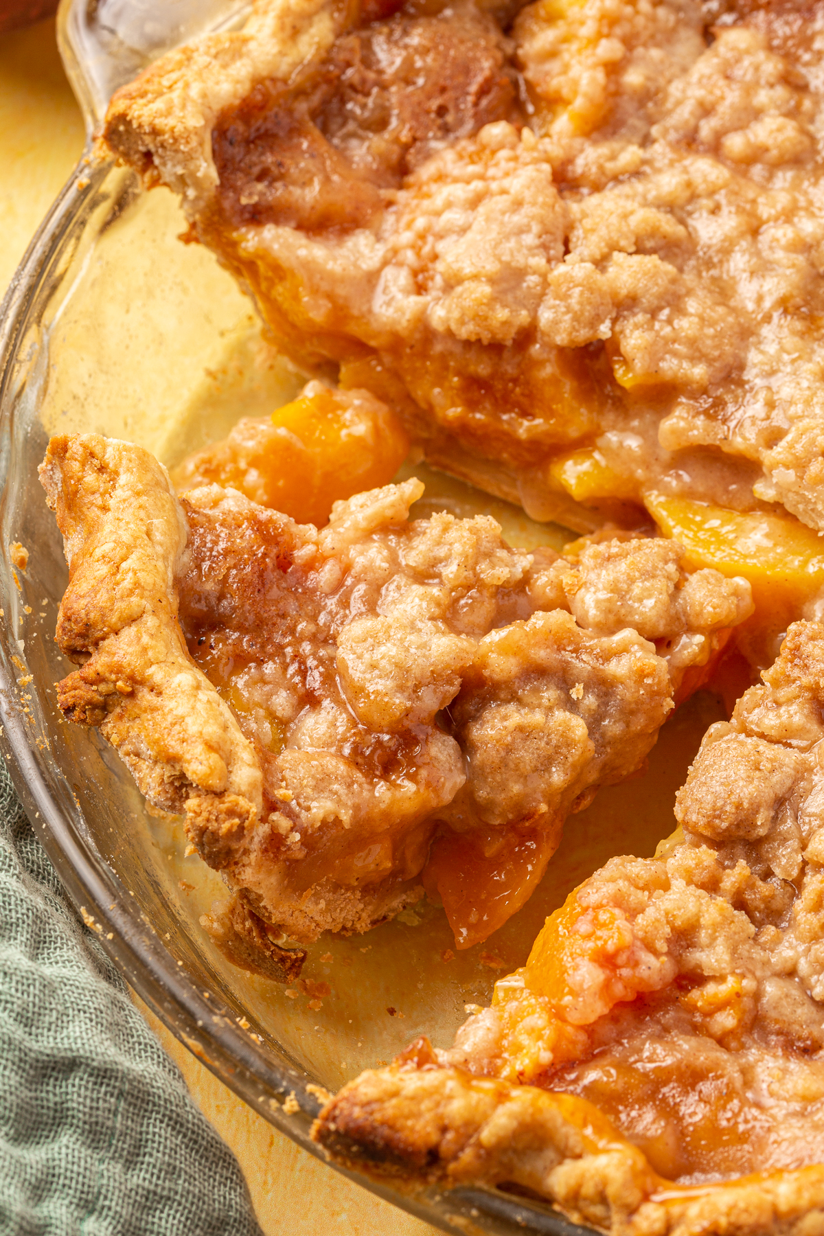 A slice of gluten-free peach crumble pie in the pie dish, next to other slices with a golden crumble topping