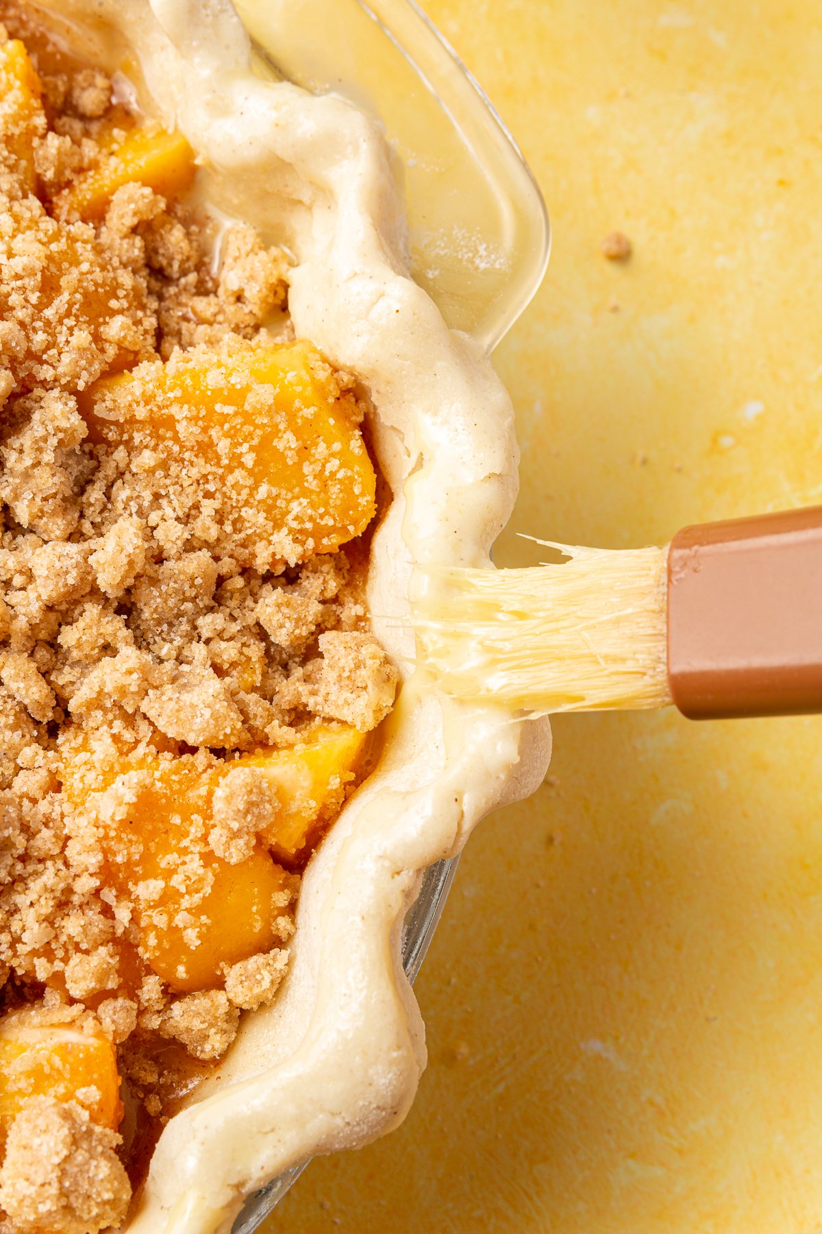 Brushing the crust of the unbaked peach crumble pie with egg wash.