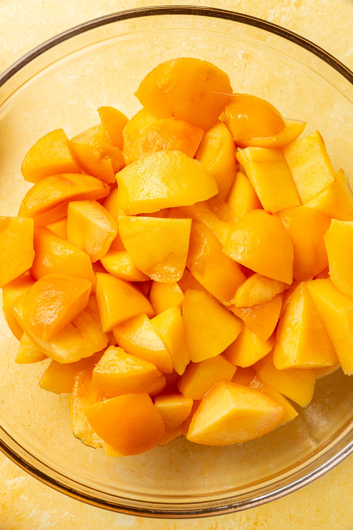 Chopped fresh peaches in a clear glass bowl, ready to be mixed for the pie filling.
