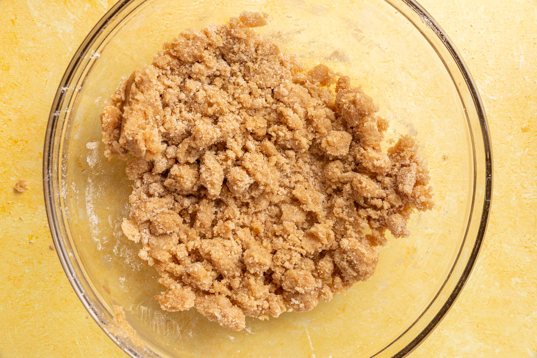 Fully mixed gluten-free crumble topping with a coarse, doughy texture in a glass bowl, ready to be added to the pie.
