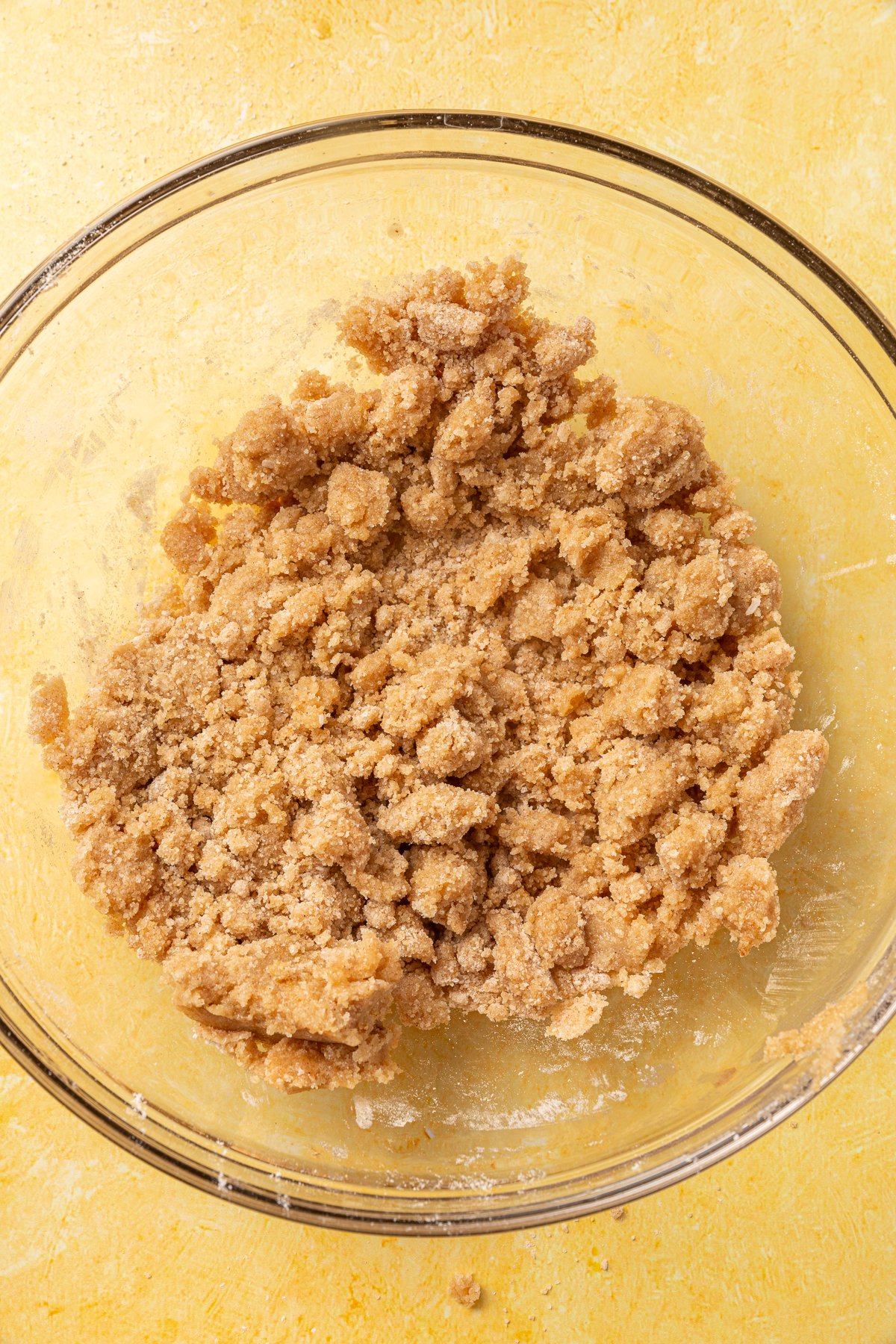 Fully mixed gluten-free crumble topping with a coarse, doughy texture in a glass bowl, ready to be added to the pie.