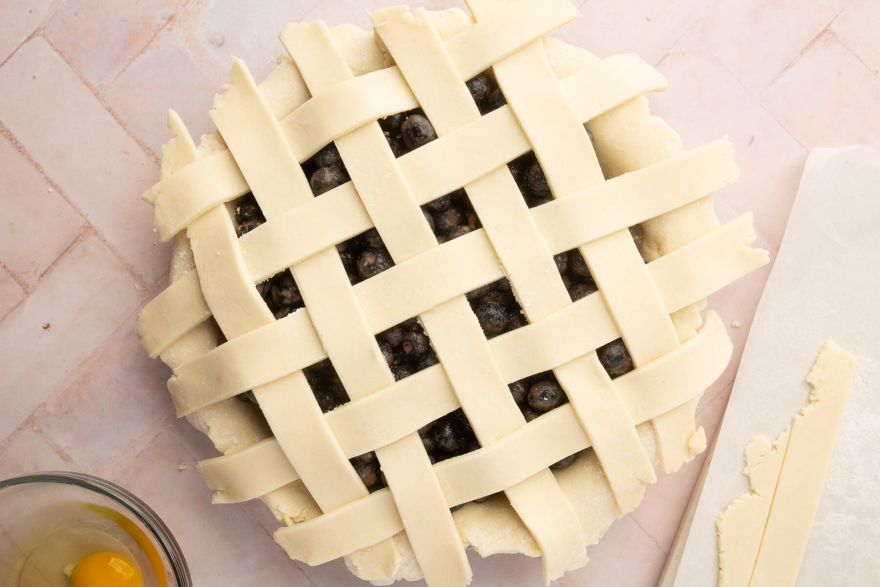 The gluten-free lattice top fully assembled over the blueberry pie filling, with an egg wash on the side for brushing.