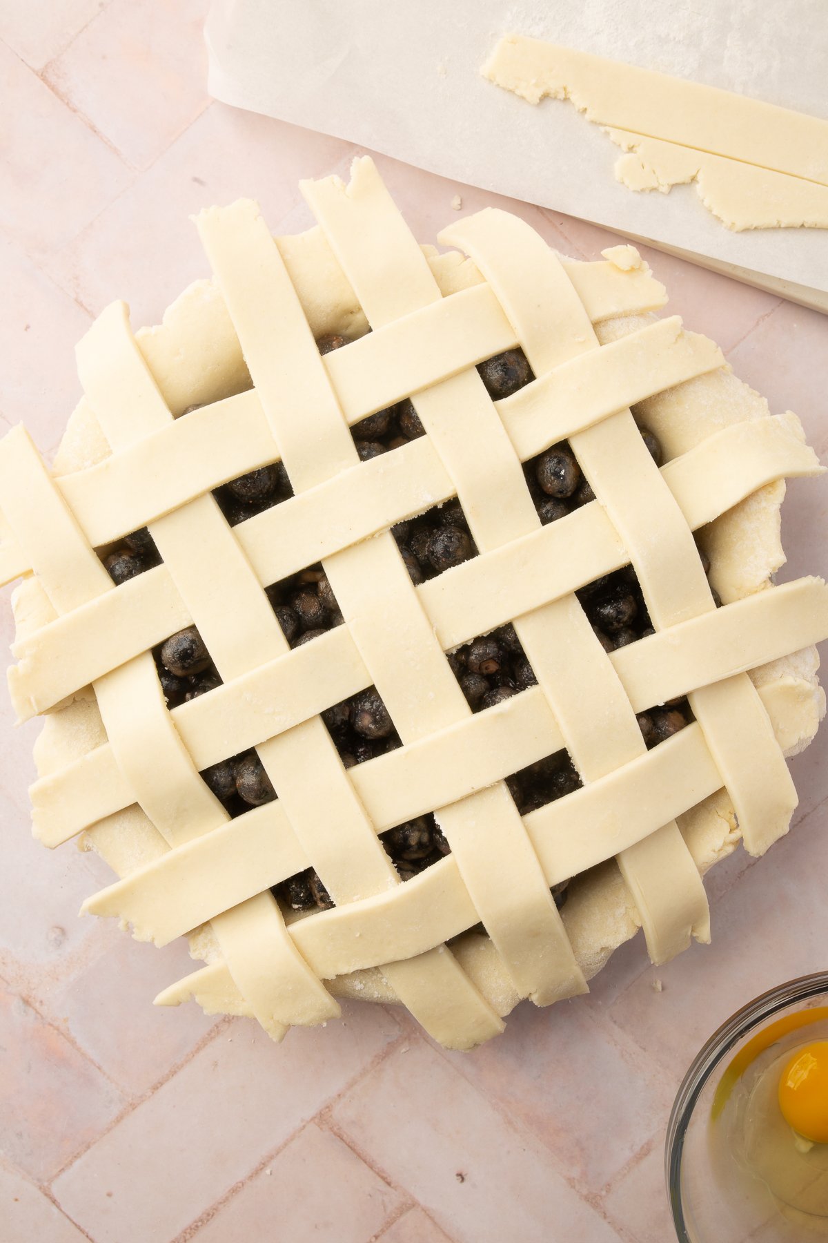 The gluten-free lattice top fully assembled over the blueberry pie filling, with an egg wash on the side for brushing.