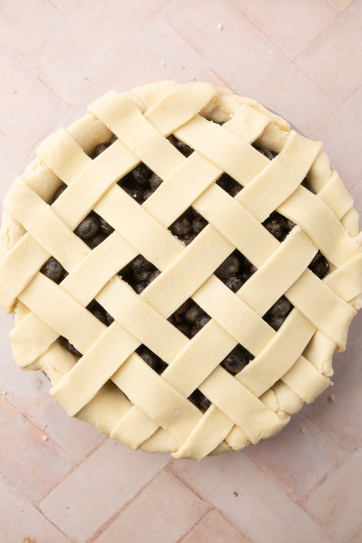 A completed lattice crust, unbaked, covering the blueberry pie filling in a pie dish.