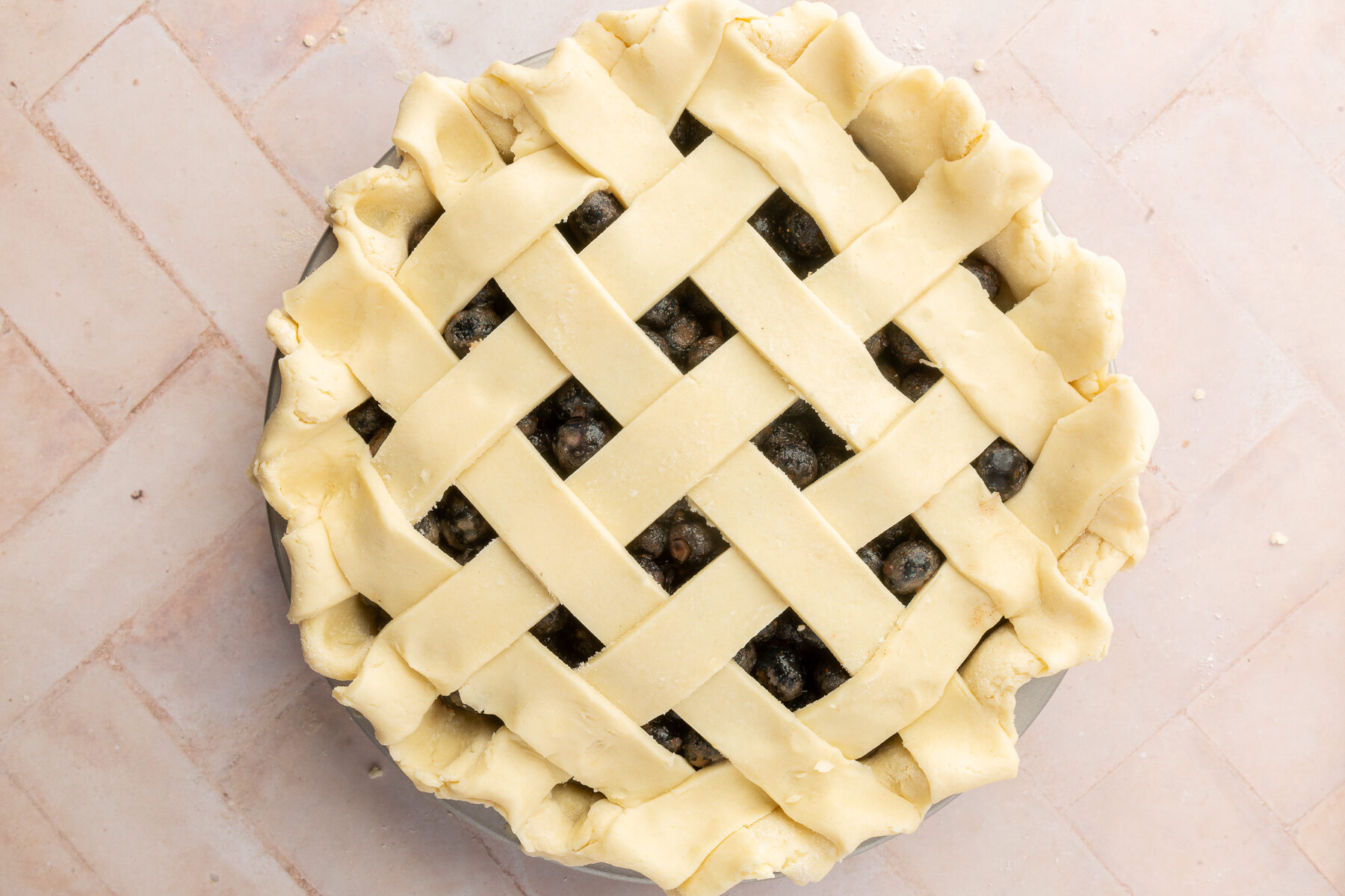 The gluten-free lattice top fully assembled over the blueberry pie filling with the edges crimped into a wavy pattern.