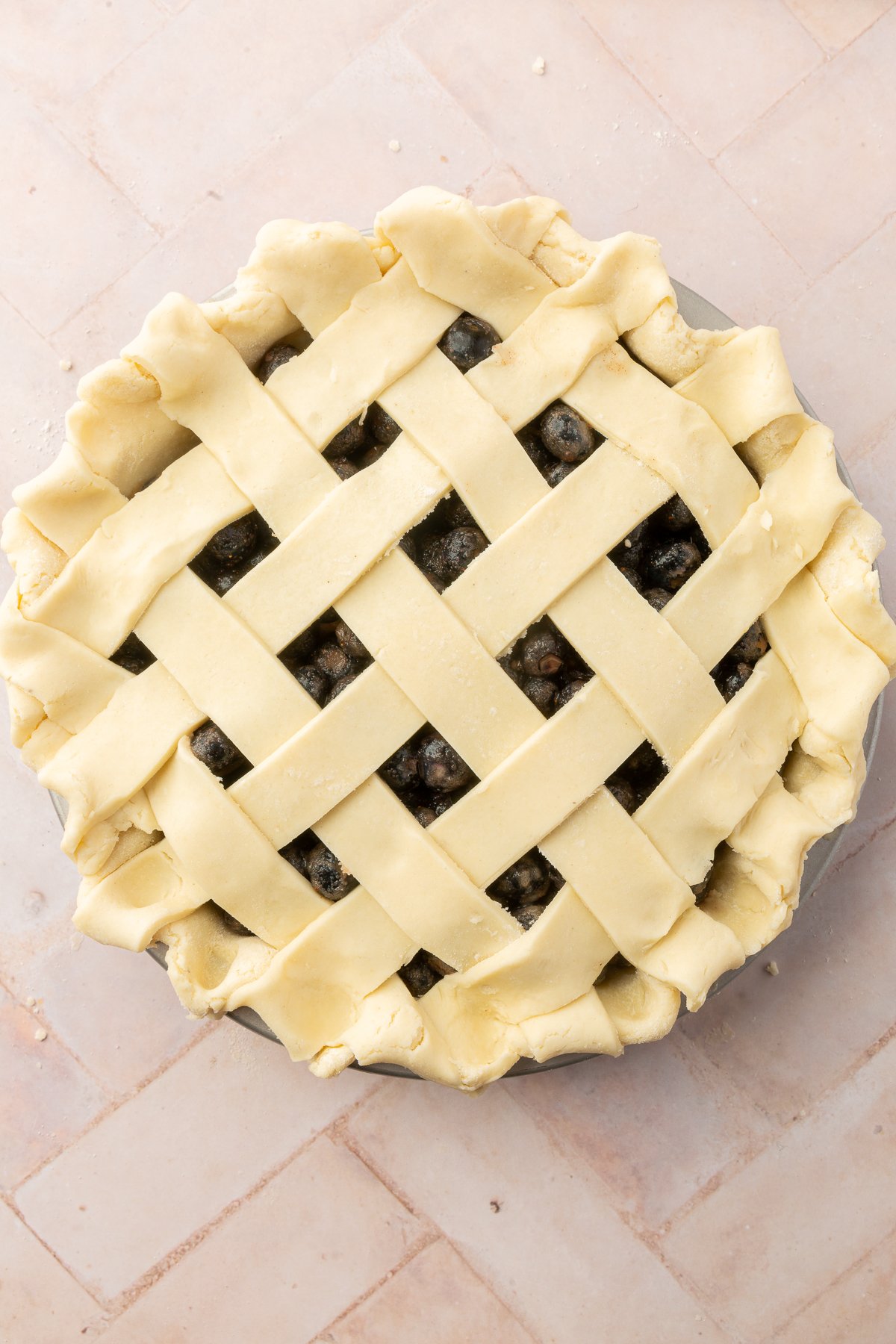 The gluten-free lattice top fully assembled over the blueberry pie filling with the edges crimped into a wavy pattern.