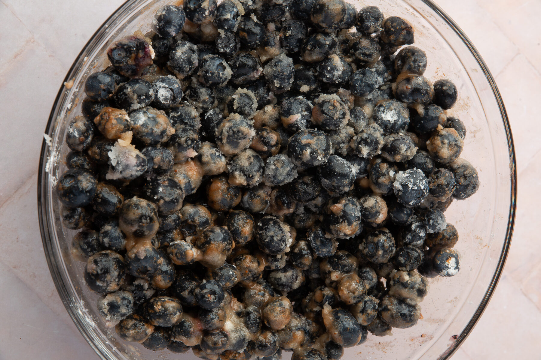 Blueberries mixed with sugar, cinnamon, and cornstarch in a glass bowl, creating a thick, coated blueberry filling for the pie.