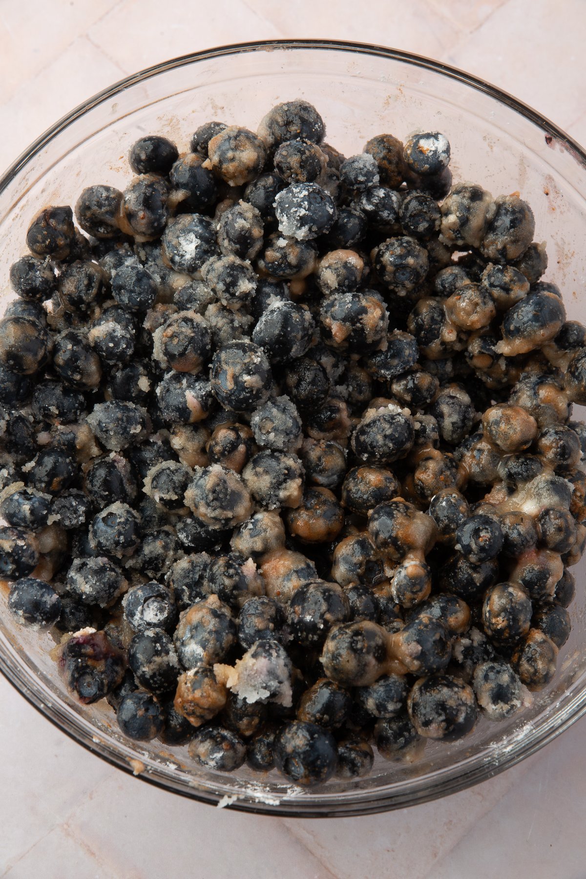 Blueberries mixed with sugar, cinnamon, and cornstarch in a glass bowl, creating a thick, coated blueberry filling for the pie.