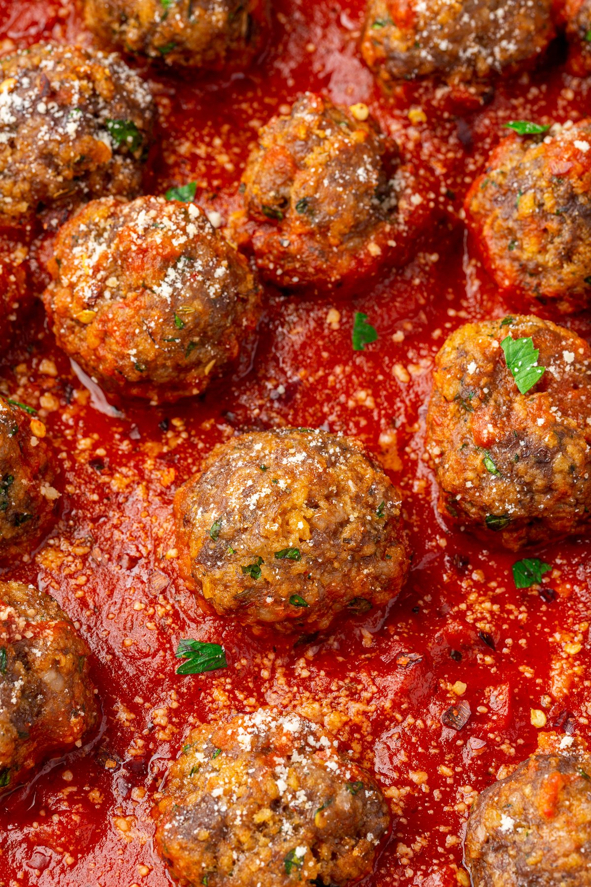 Close up image of spicy ground beef, Italian sausage, and gluten-free breadcrumb meatballs resting in a red marinara sauce.