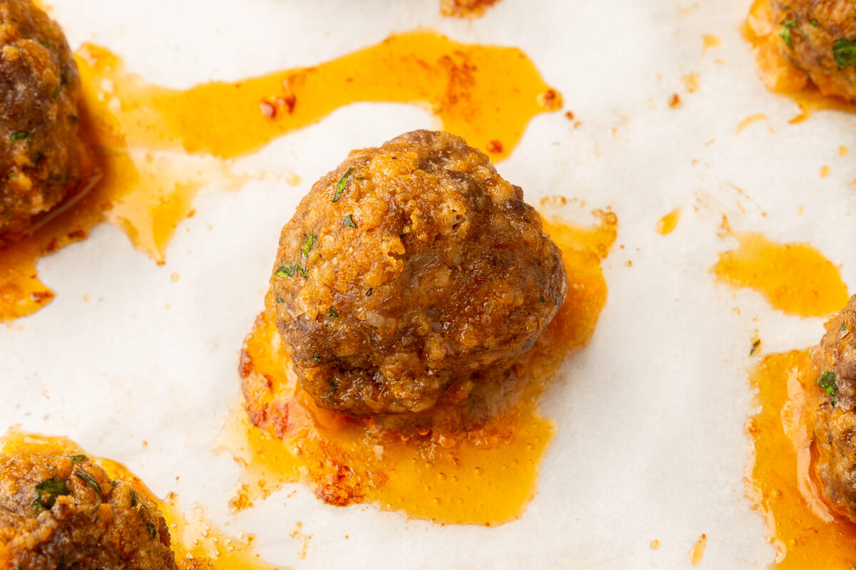 Close up image of spicy meatballs on parchment paper on a baking sheet right after being taken out of the oven.